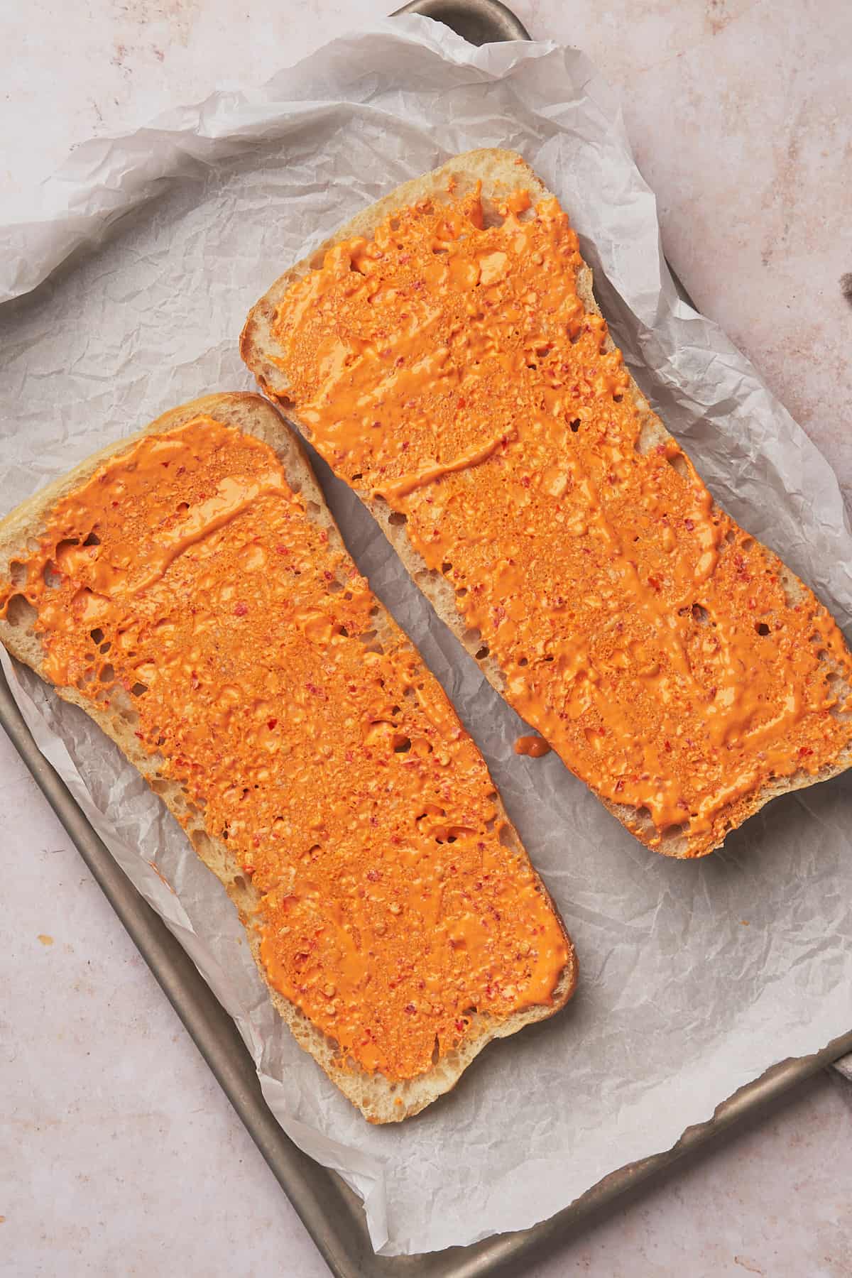 a loaf of ciabatta bread cut in half on a baking sheet, slathered in Calabrian chili mayo. 