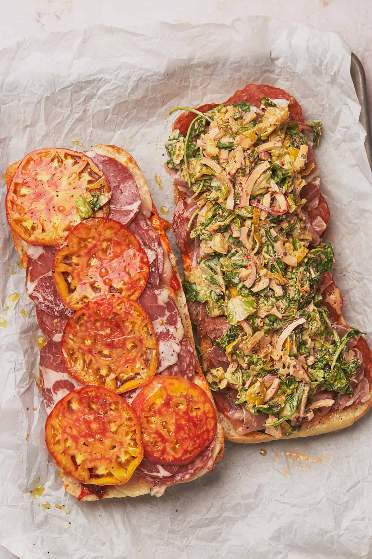 italian sub with grinder salad, heirloom tomatoes, meats, and cheeses open before being put together and cut. 