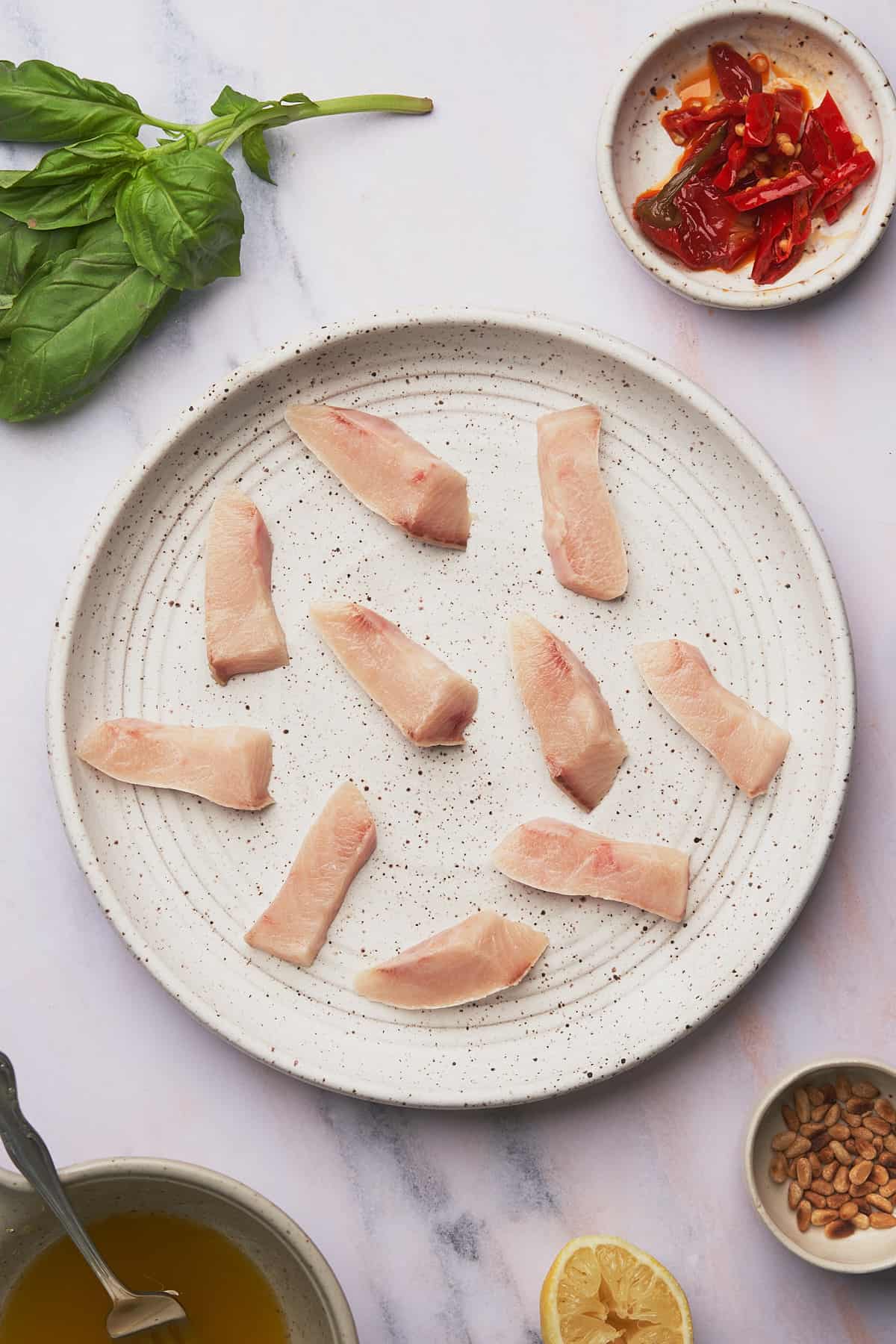 sliced raw hamachi on ceramic white textured plate, surrounded by ingredients to make hamachi crudo. 