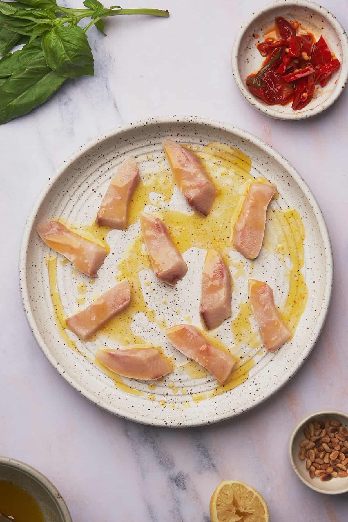 raw yellowtail fish coated in an olive oil, lemon juice sauce on a white textured ceramic plate. 