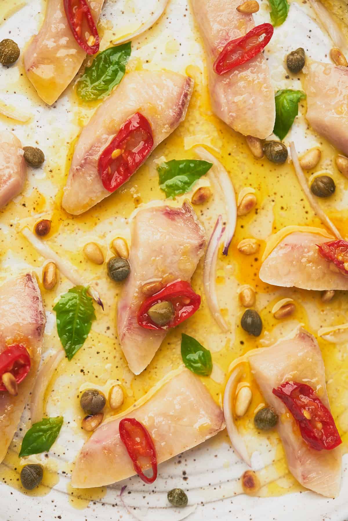 close up shot of thin slices of raw hamachi with lemon juice, olive oil, chiilis, and basil on a ceramic speckled plate.