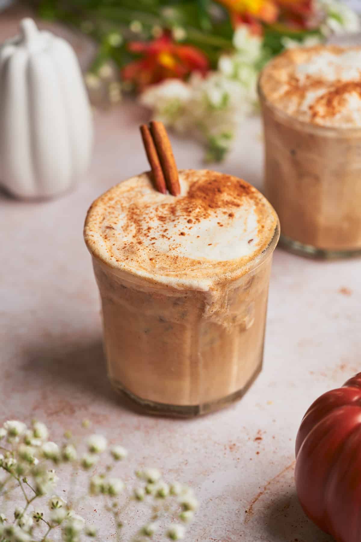 iced pumpkin spice latte, with white ceramic pumpkins in the back, and wild flowers. 