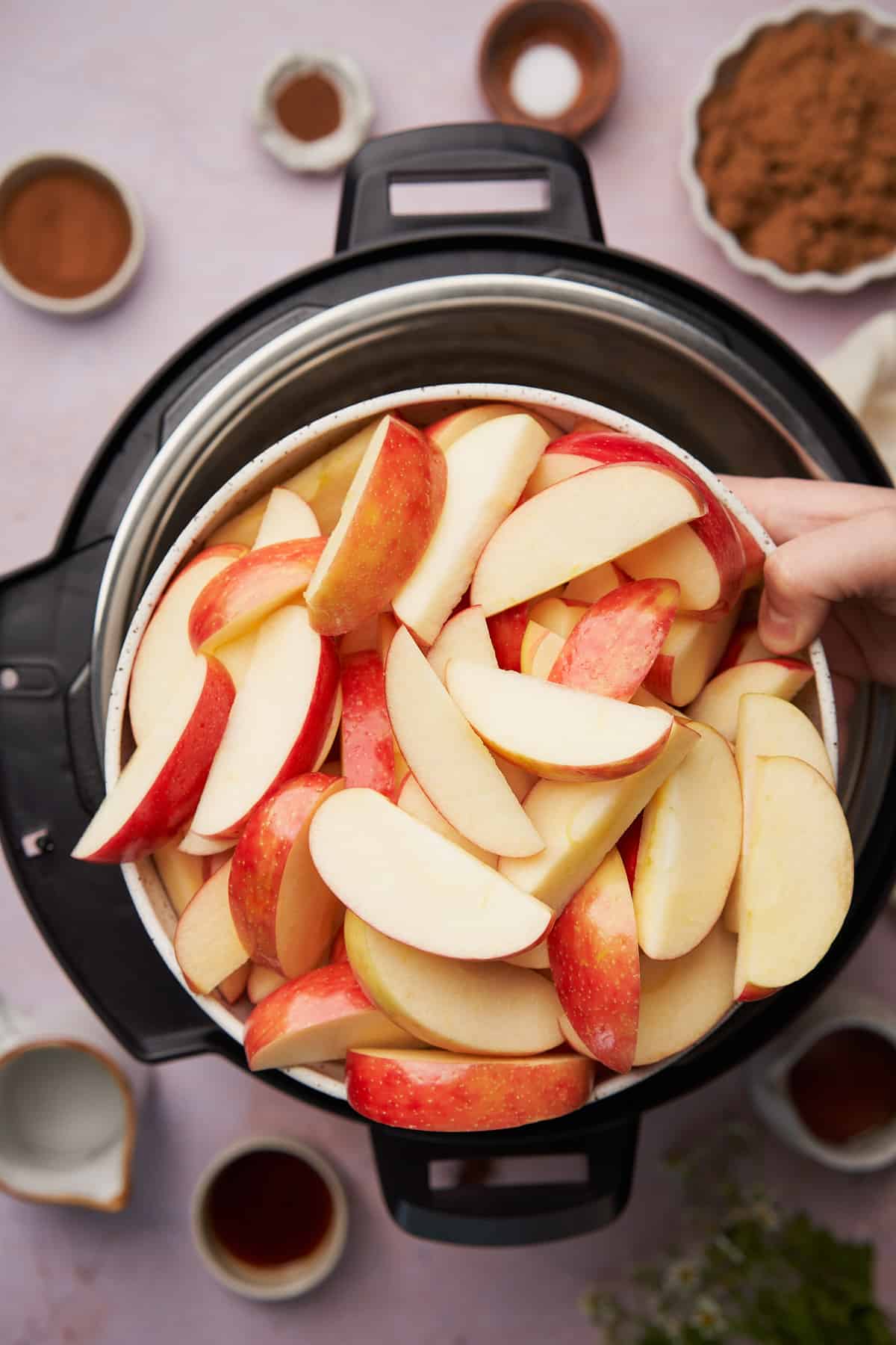 hands holding a large bowl of cut up apples. 