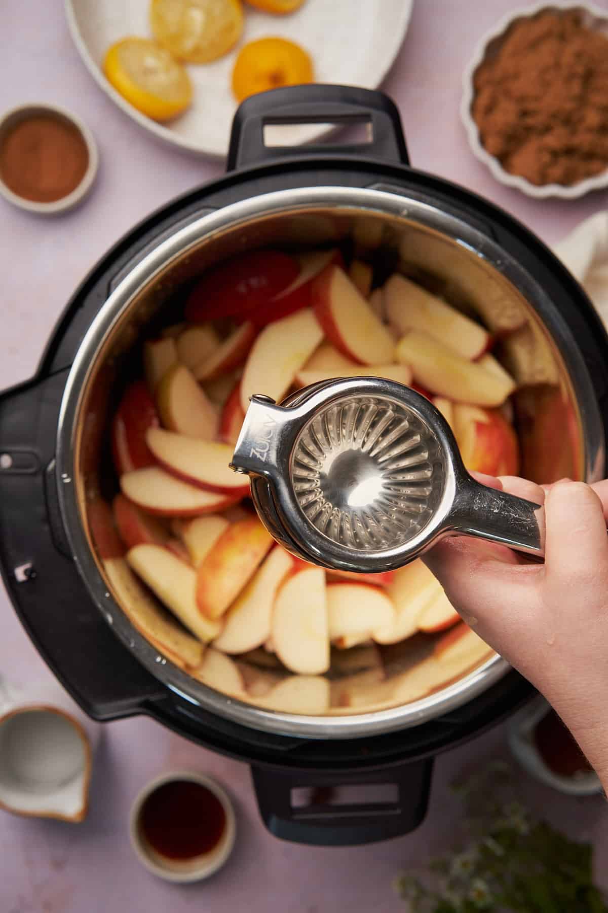 hand squeezing a citrus squeezer over top of the instant pot full of apple slices.