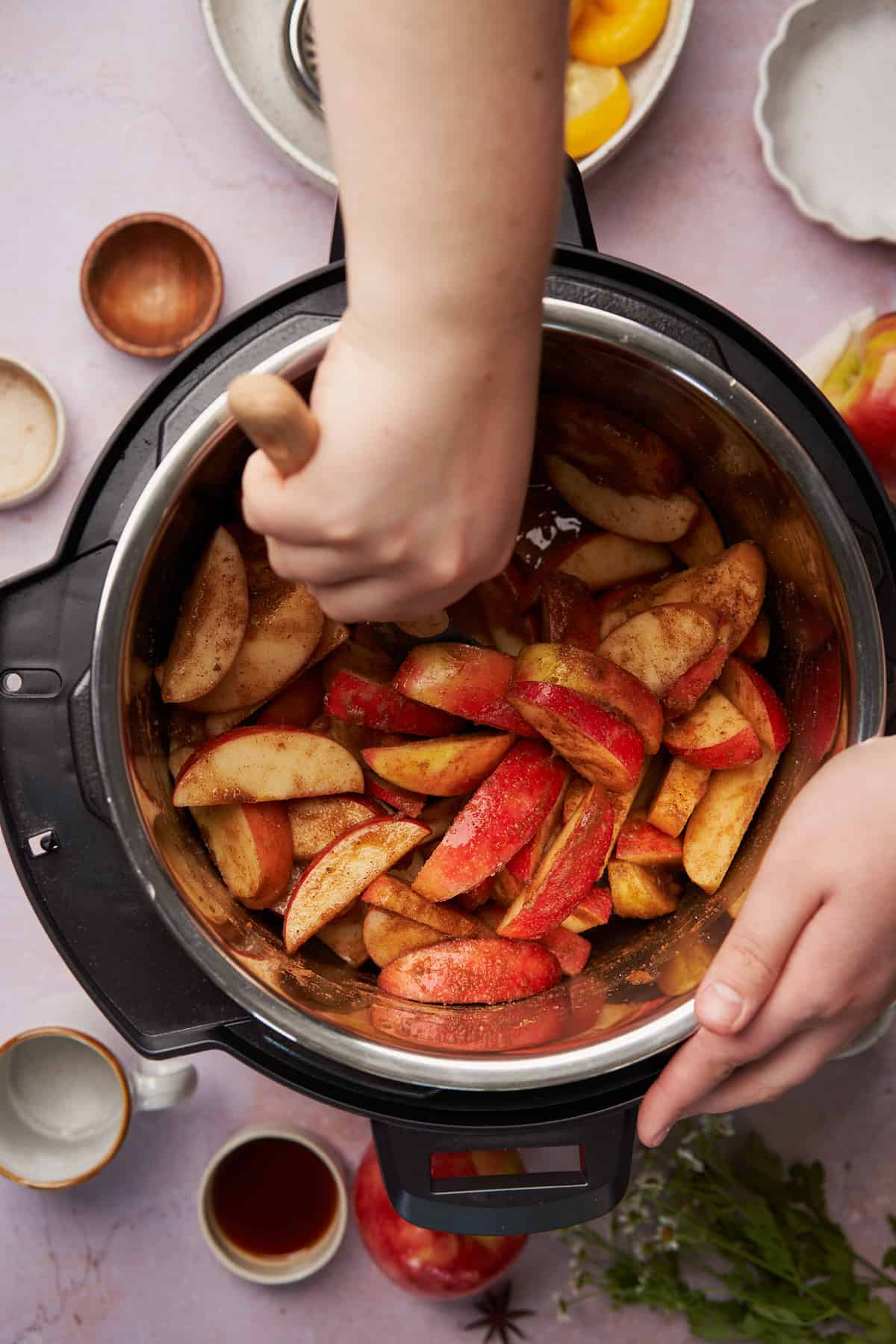 hand using a wooden spoon to stir the apple and spice mixture in an instant pot. 