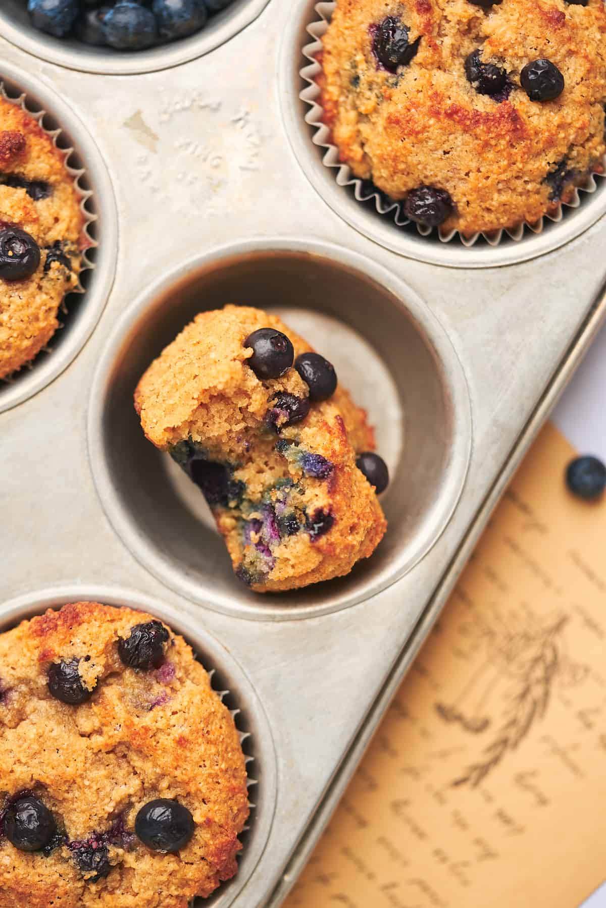 the inside of a keto blueberry muffin showing because a bite was taken out, with the muffin sitting in a tin surrounded by other muffins.  