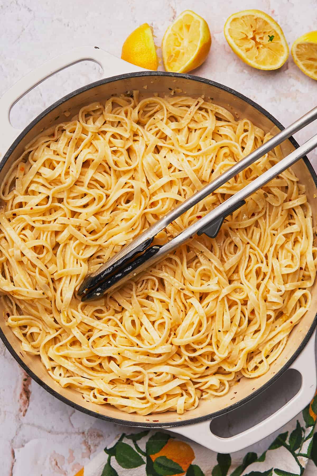 cooked linguine noodles with rubber tongs in an enameled cast iron skillet. 