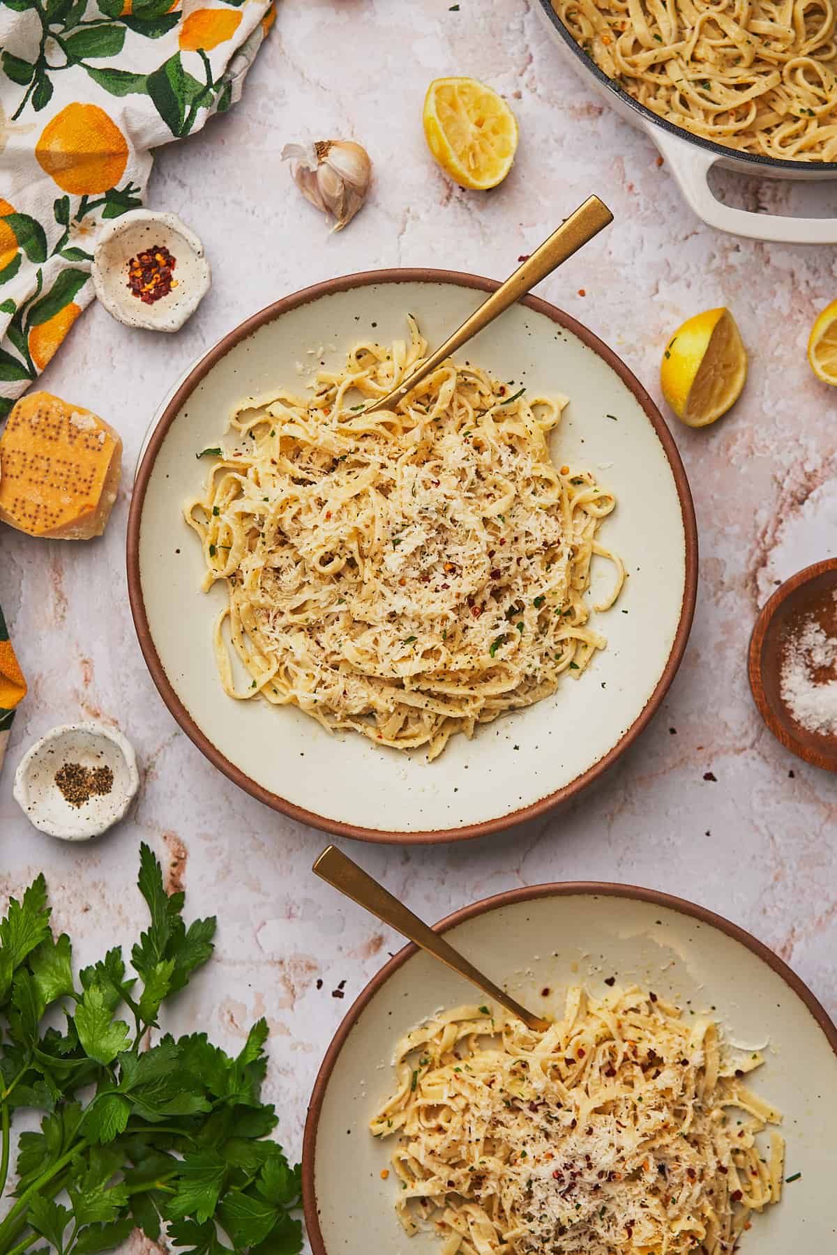 two shallow bowls full of linguine topped with lemon garlic butter pasta, with parsley and fresh parmesan. 