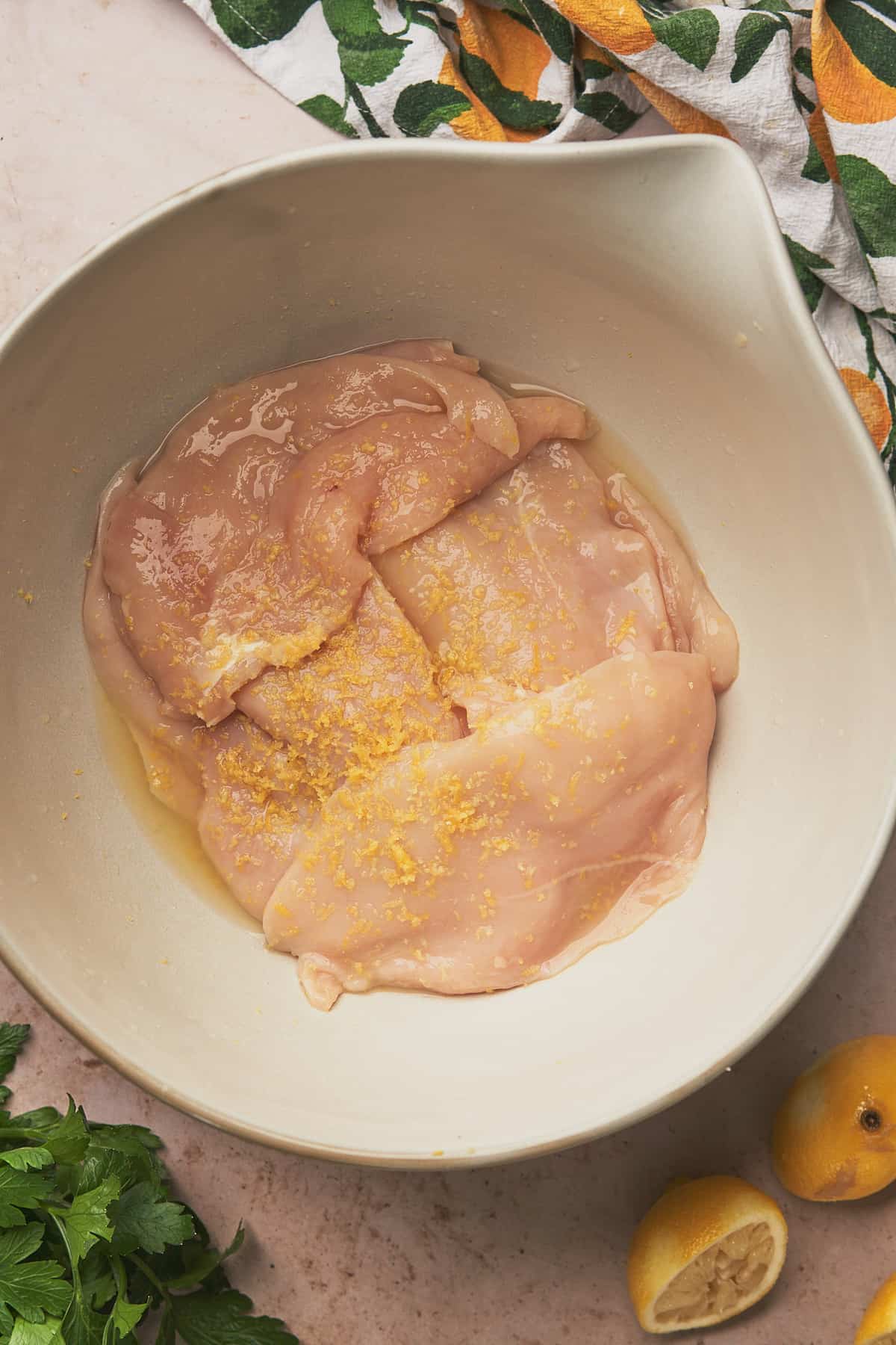 raw chicken breasts in a white ceramic bowl covered in lemon juice and zest.