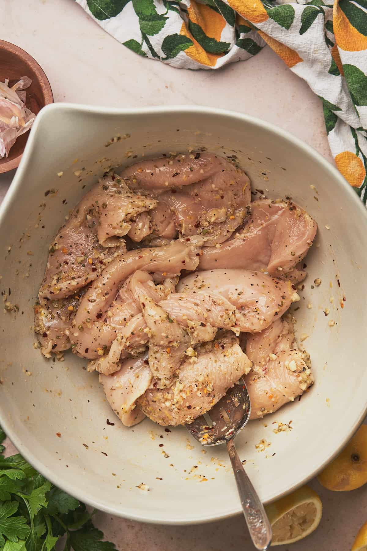 raw chicken in a large ceramic bowl tossed with seasonings, garlic, and lemon. 