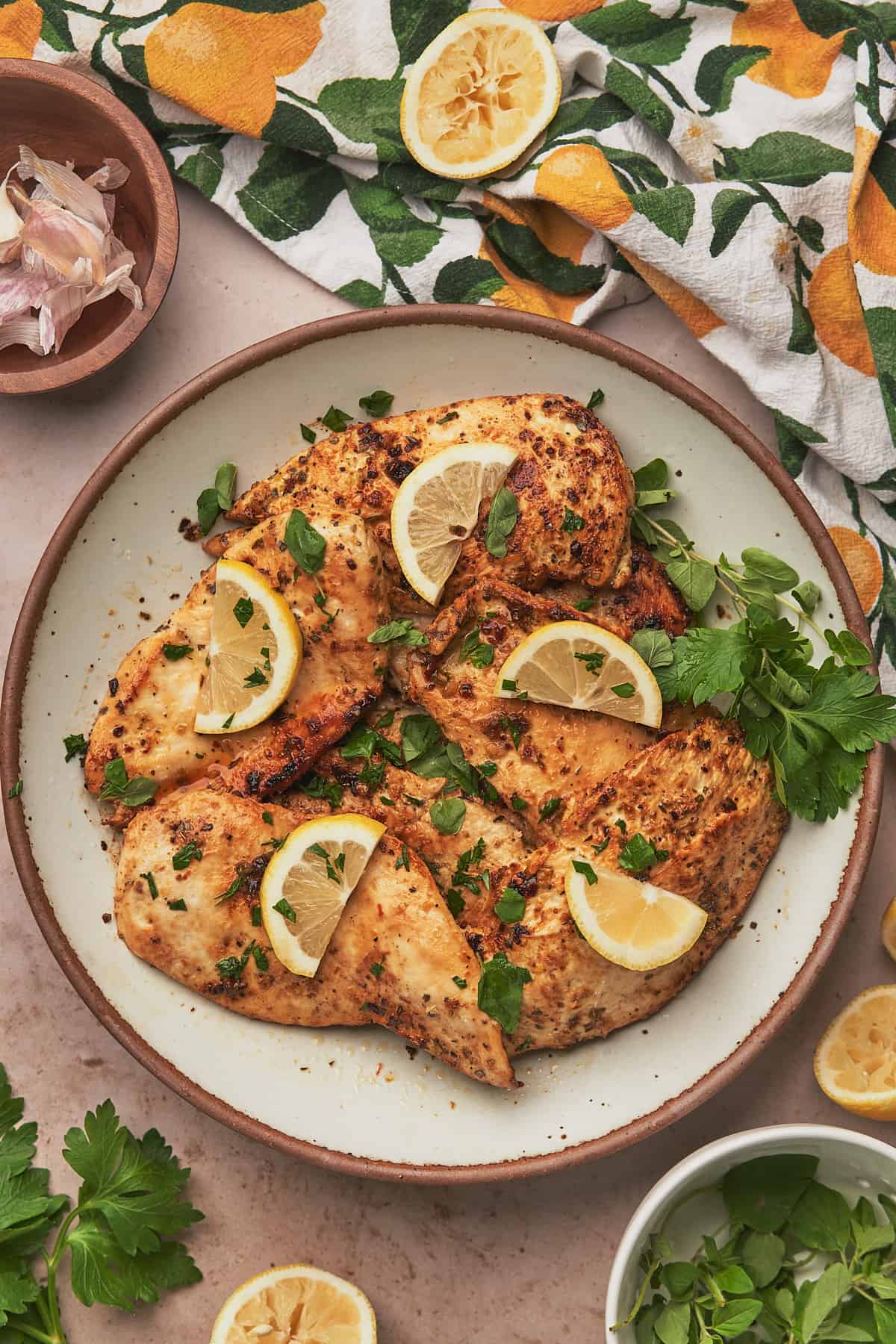 lemon herb chicken on a plate with fresh parsley, oregano, and lemon slices. 