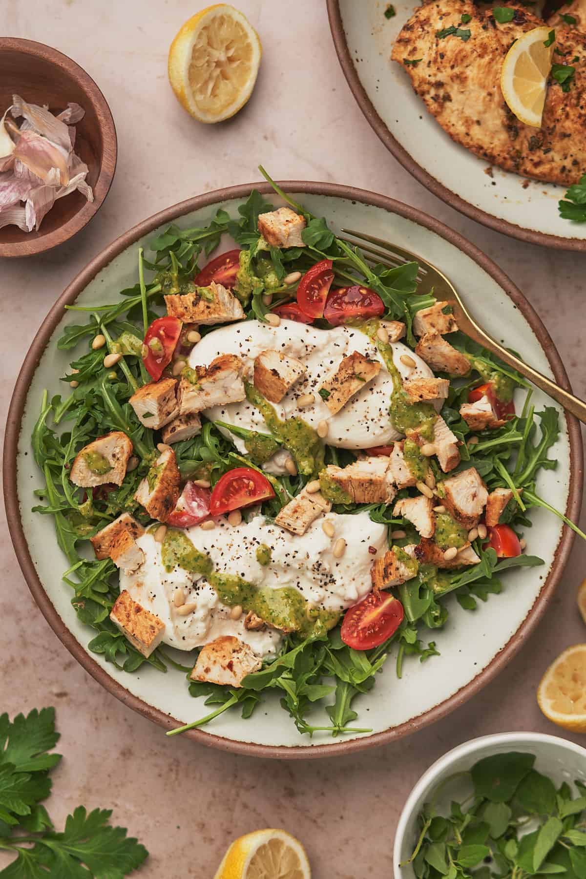 burrata salad topped with chicken pieces, tomatoes, and pesto dressing.