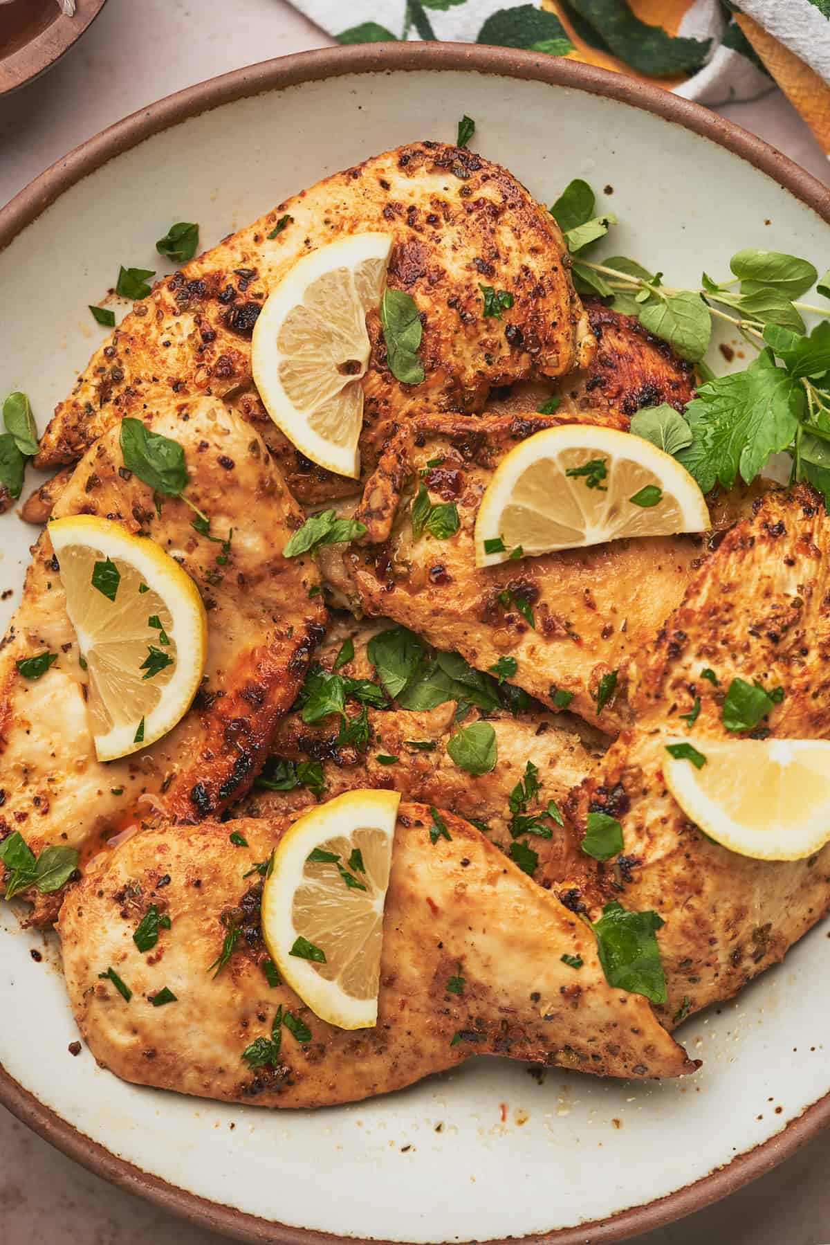 plate full of cooked chicken breasts topped with lemon slices and fresh herbs. 