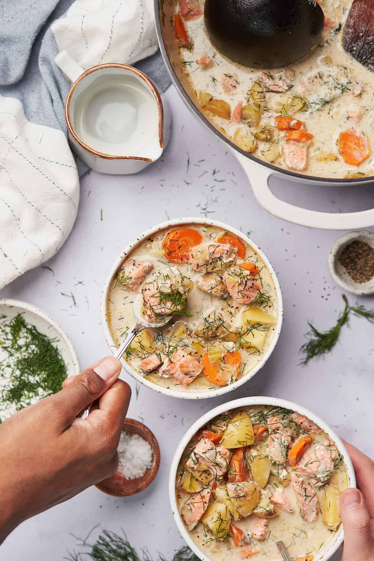 hand reaching into a bowl of creamy salmon chowder topped with fresh dill.