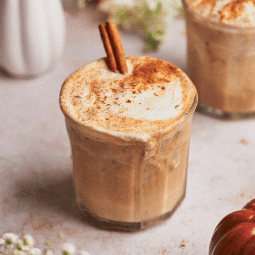 pumpkin spice iced latte with baby's breath flowers, a cinnamon stick, and ceramic pumpkins surrounding it.