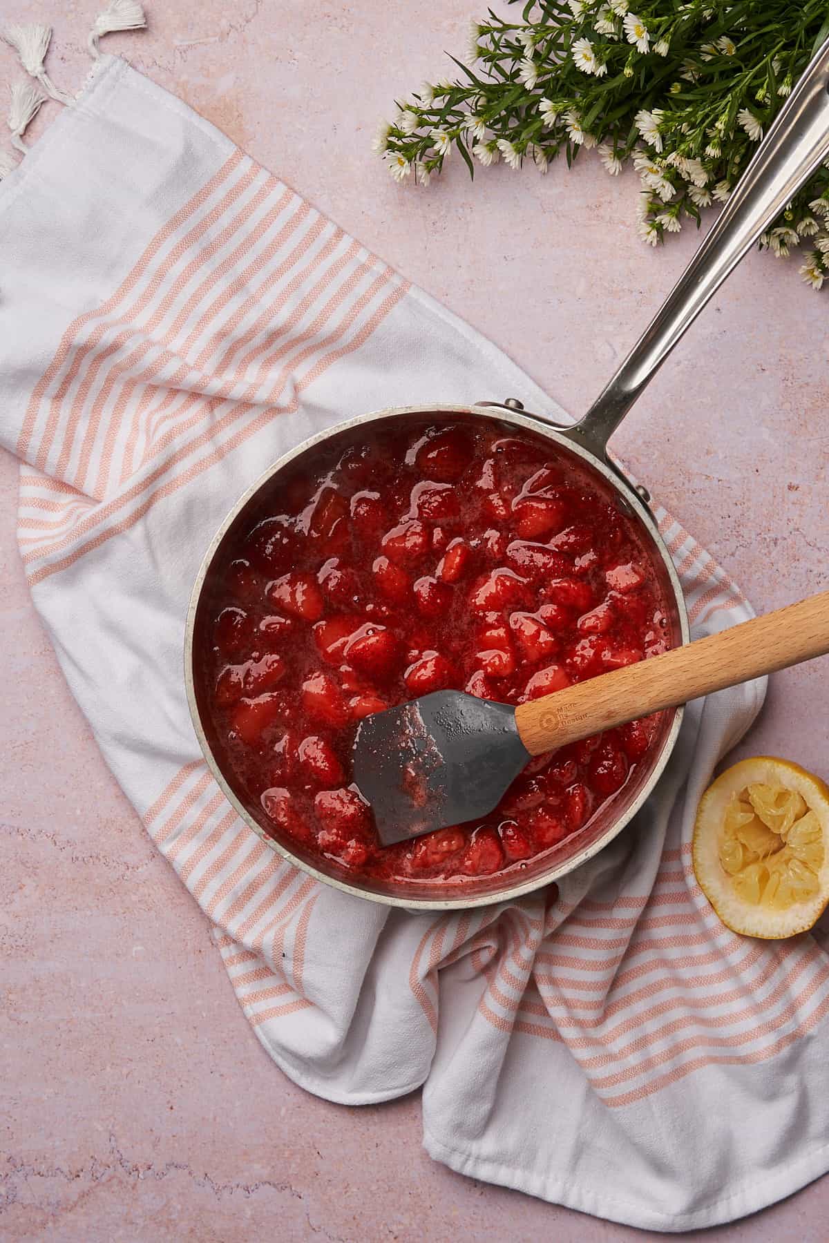fresh made strawberry sauce in a saucepan, over top of a pink striped linen towel. 