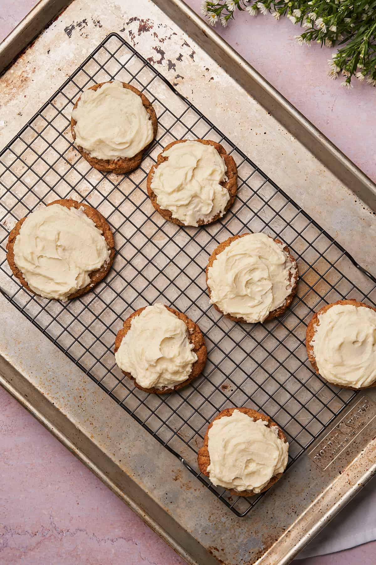 cookies on a cooling rack and baking sheet topped with cream cheese frosting. 
