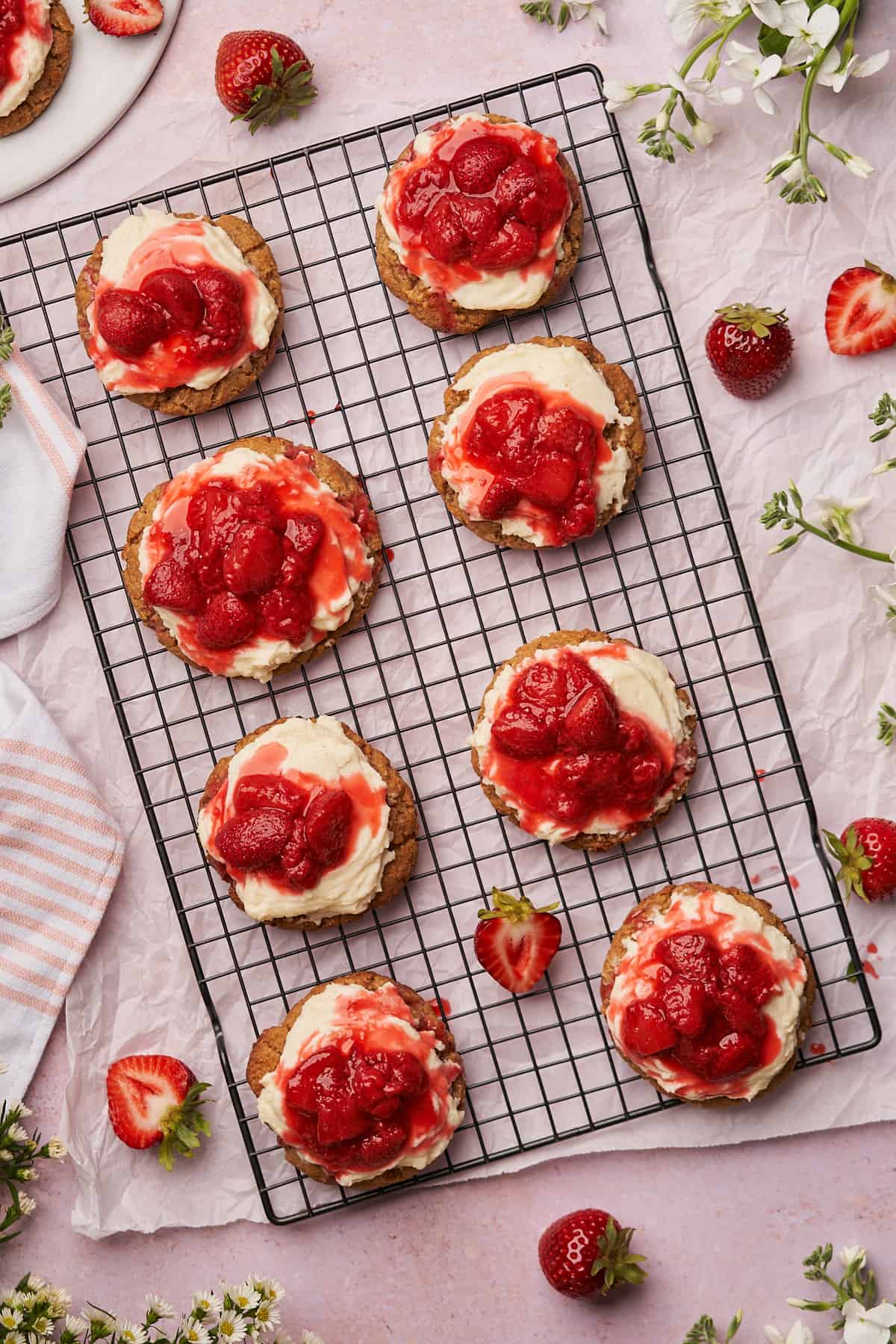 cookies topped with cream cheese frosting and fresh strawberry sauce on a black wire cooling rack. 