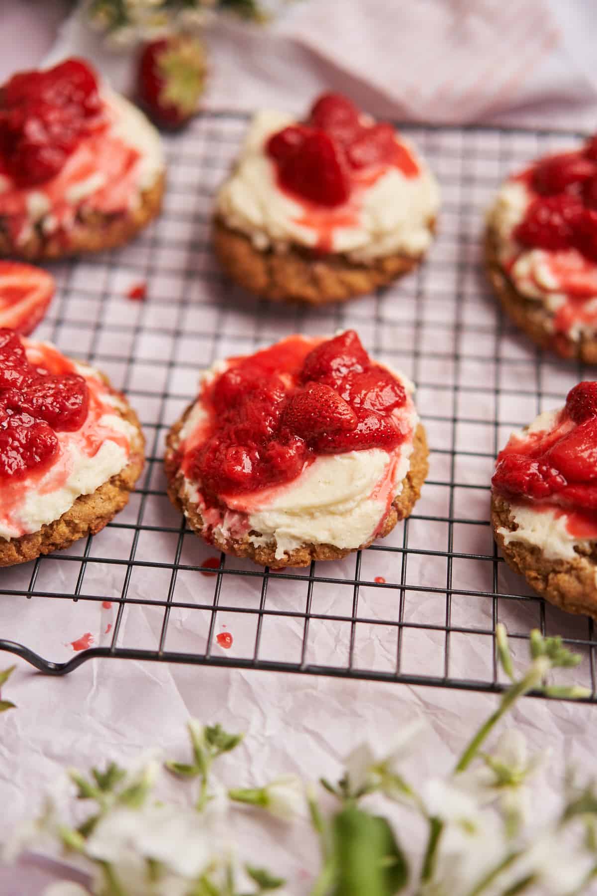 stunning photo of strawberry cheesecake cookies on a black wire cooling rack over white parchment paper. 