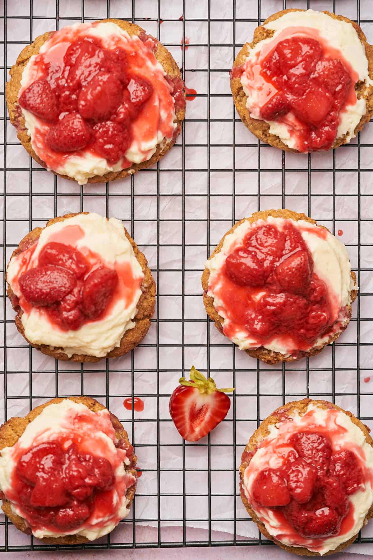 stunning shots of a row of 6 strawberry cheesecake cookies, with frosting spread over top, and fresh strawberry sauce. 