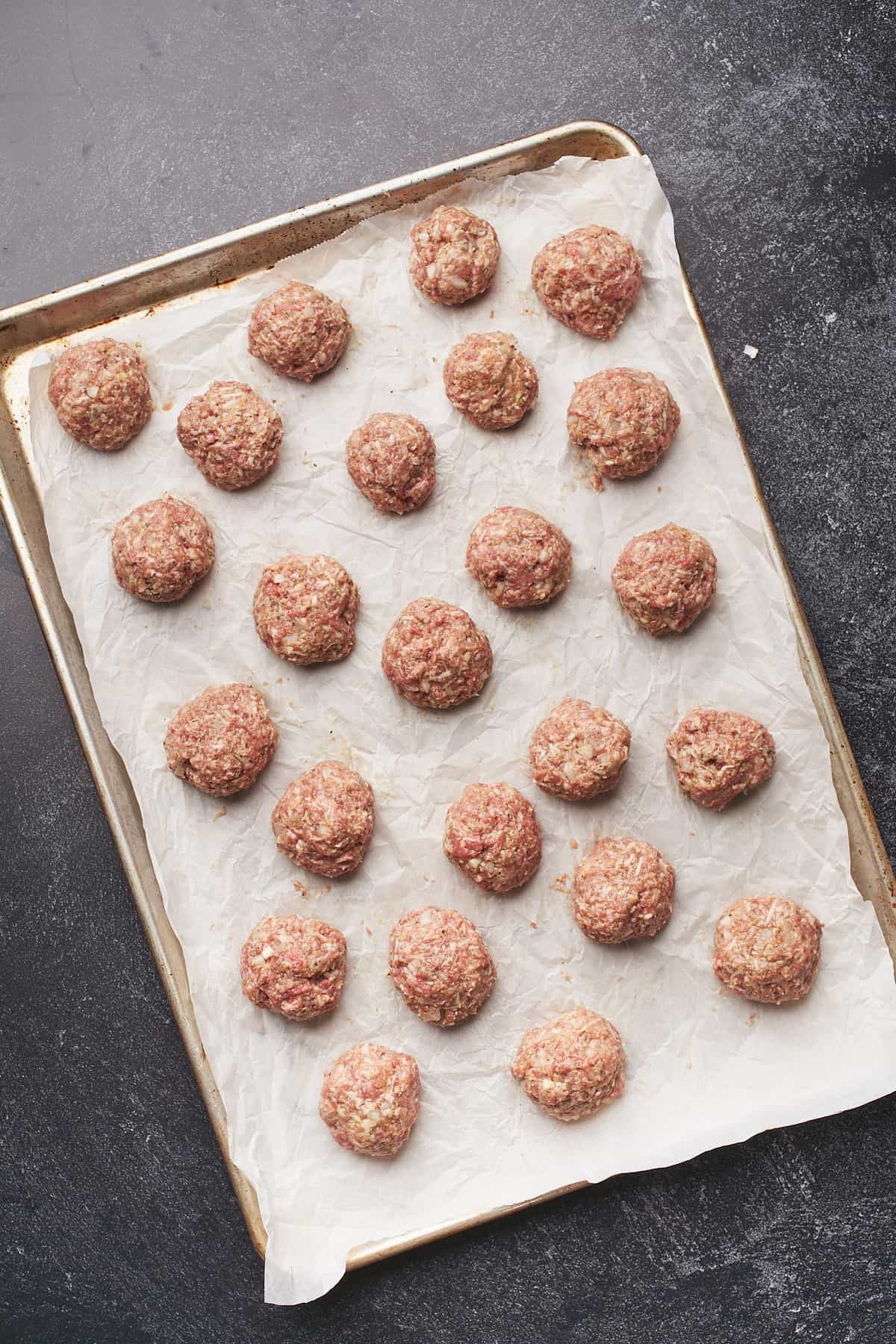 24 raw meatballs on a baking sheet.