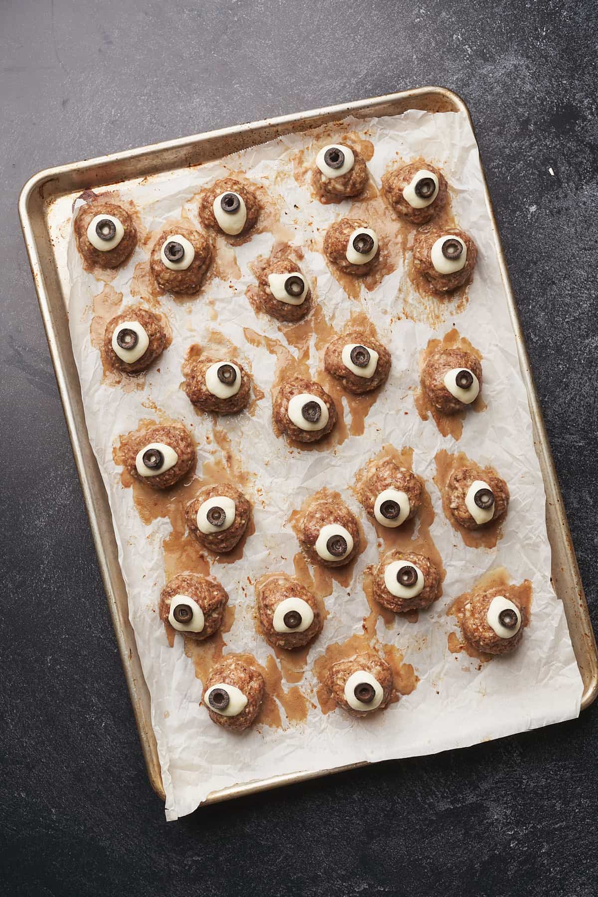 meatball eyeballs with mozzarella and olive slices on a baking sheet. 