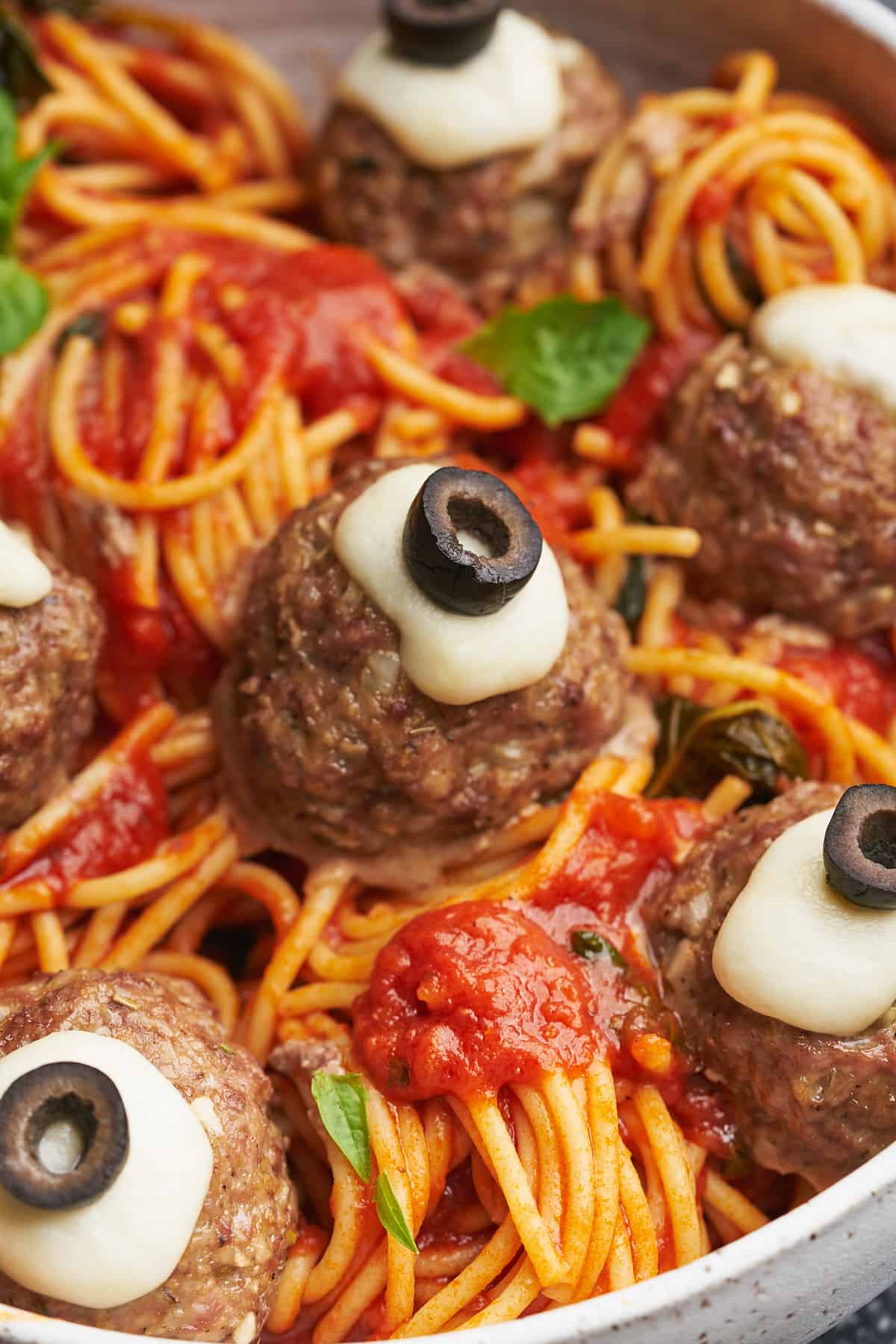 close up shot of a spaghetti and marinara with meatball eyeballs, topped with melted mozzarella and olive slices. 