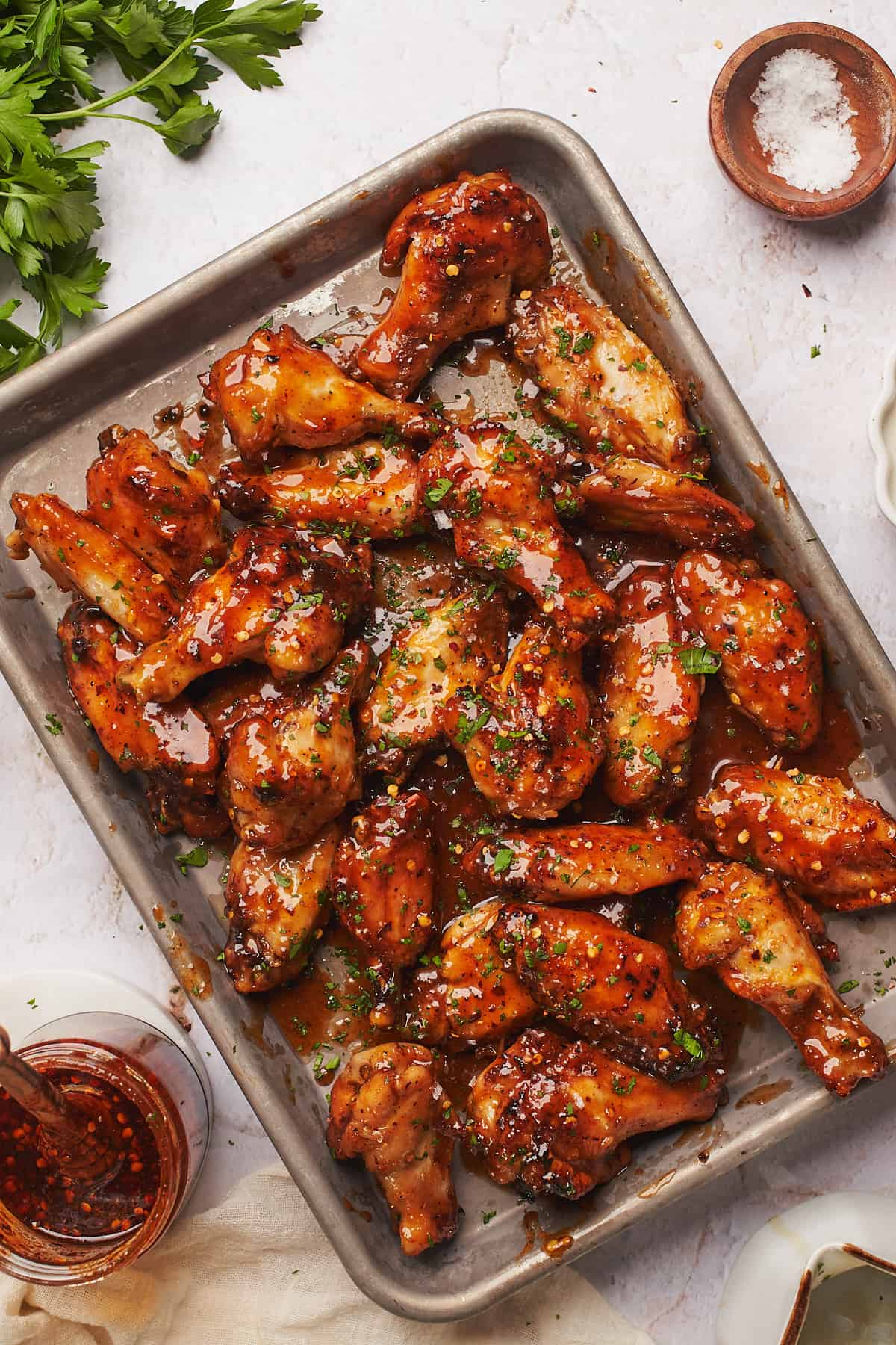 tray of hot honey chicken wings with sauce nearby, garnished with parsley. 