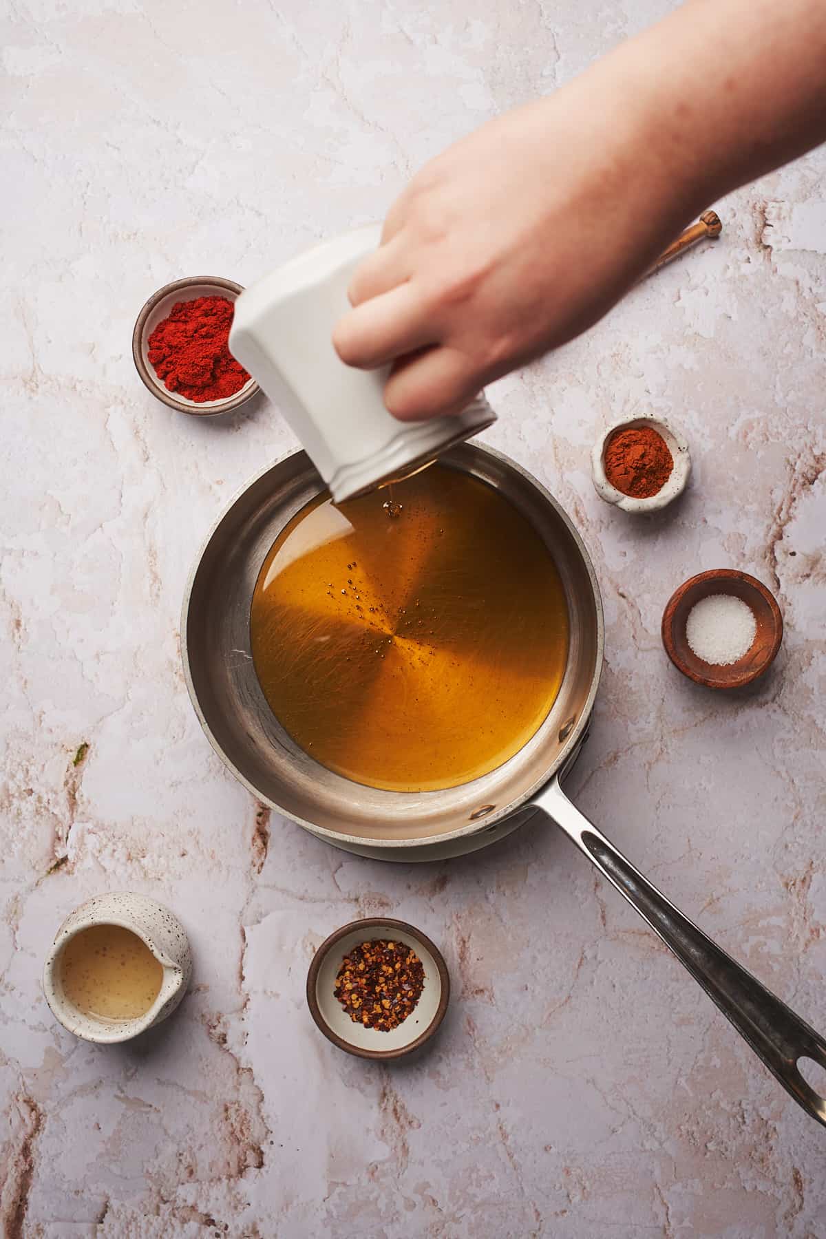 hand pouring honey into a saucepan surrounded by seasonings. 