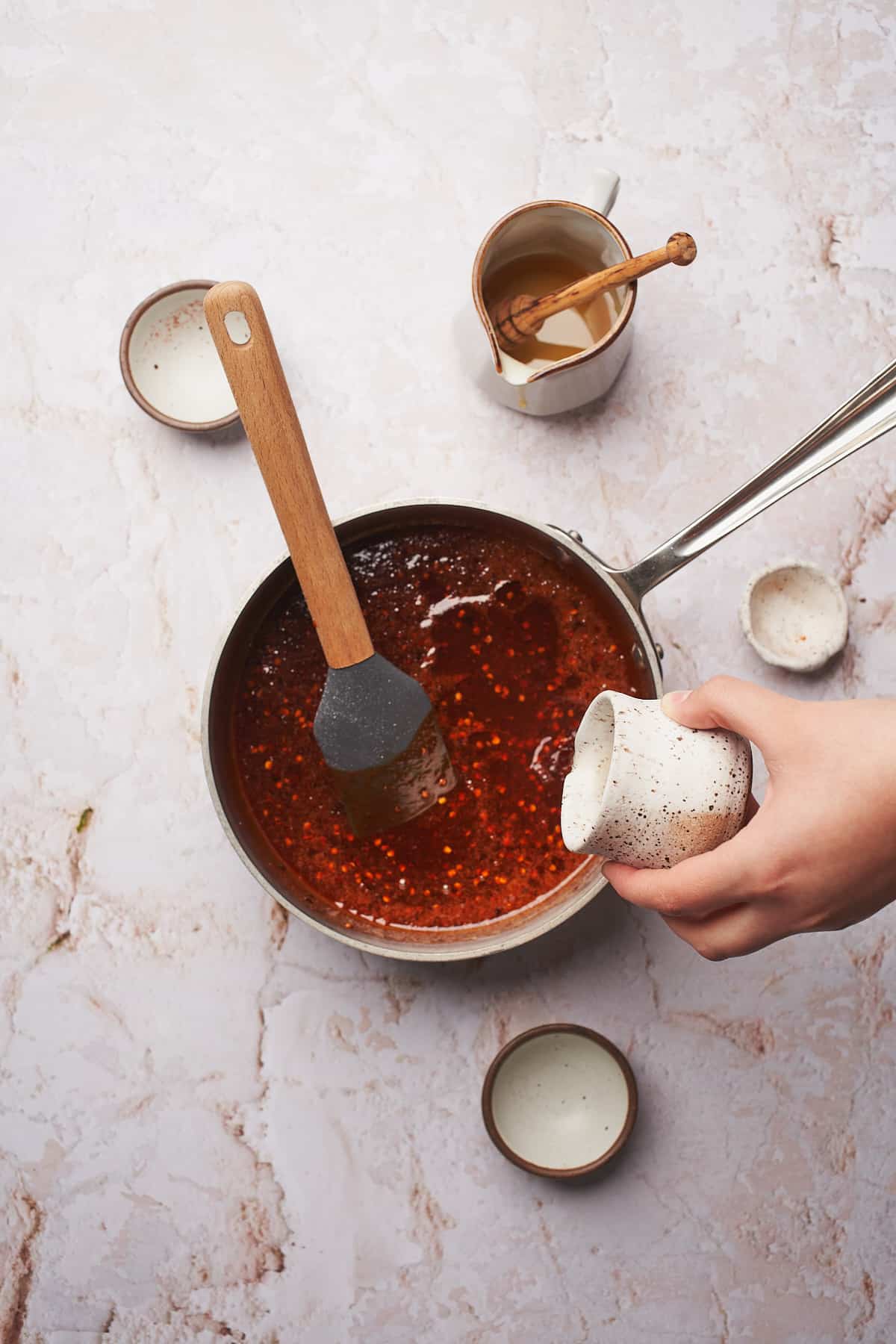 Hand pouring in vinegar into spicy honey in a saucepan saucepan. 