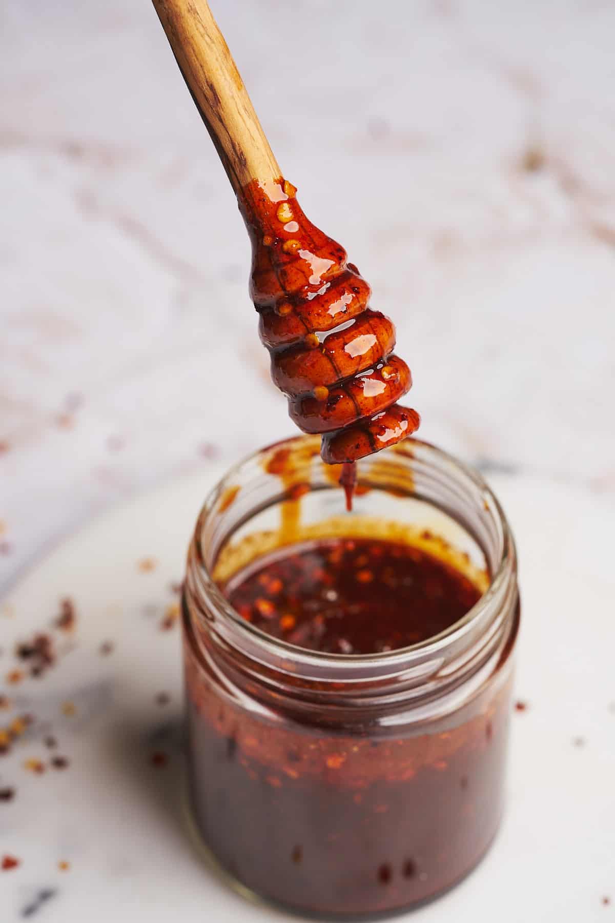 close up shot of spicy honey on a honey dripper going back into a jar. 