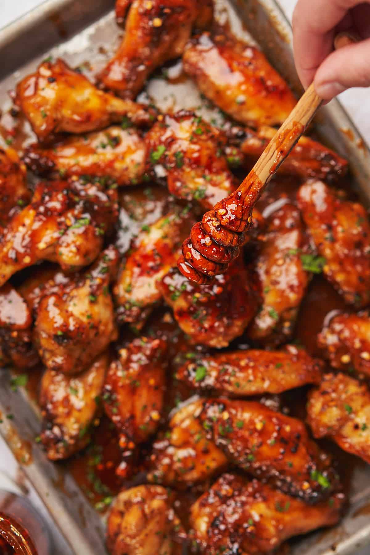 spicy hot honey sauce all over chicken wings on a baking sheet. 