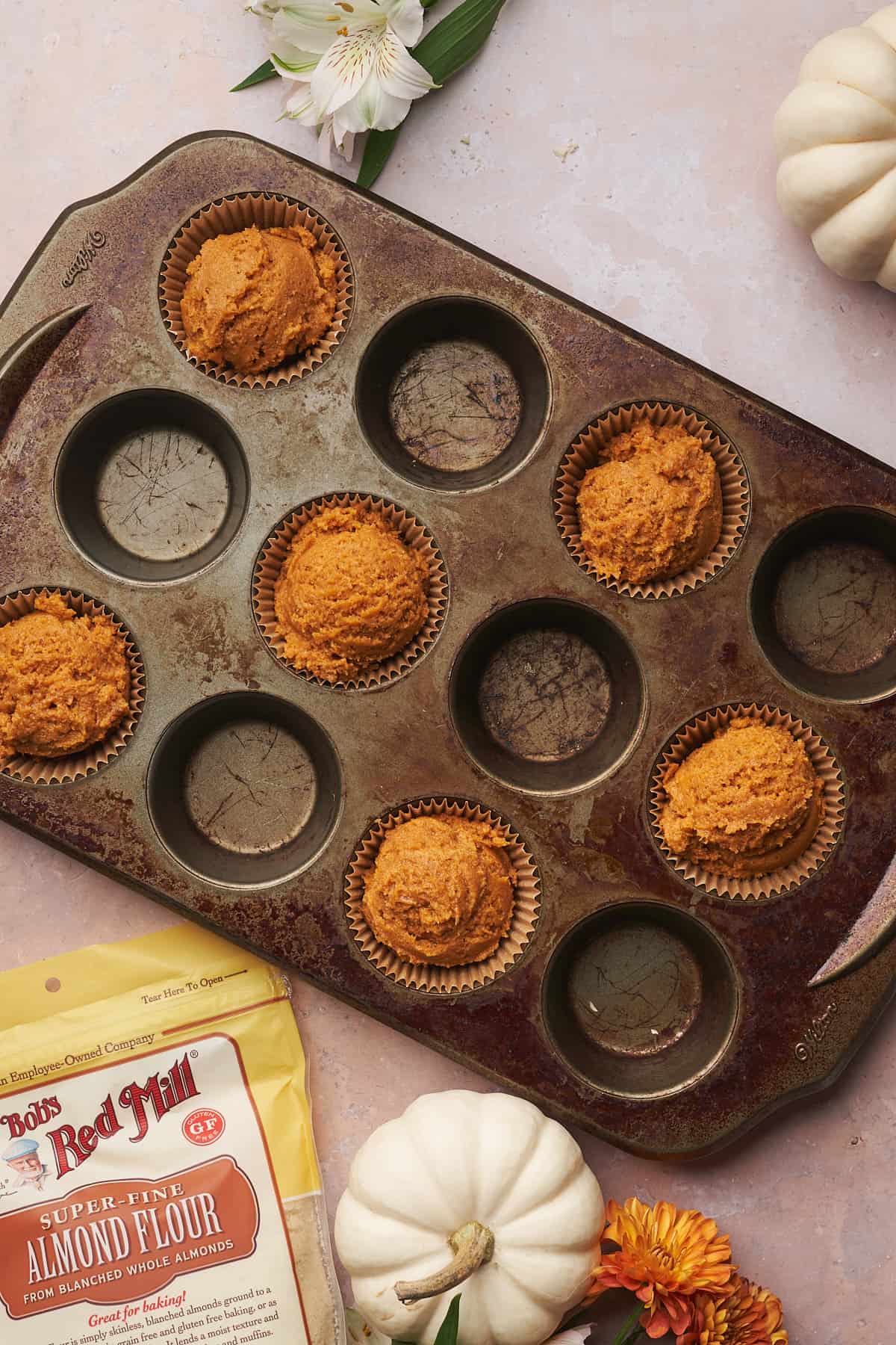 pumpkin muffin batter in a muffin tin with a bag of bob's red mill almond flour nearby. 