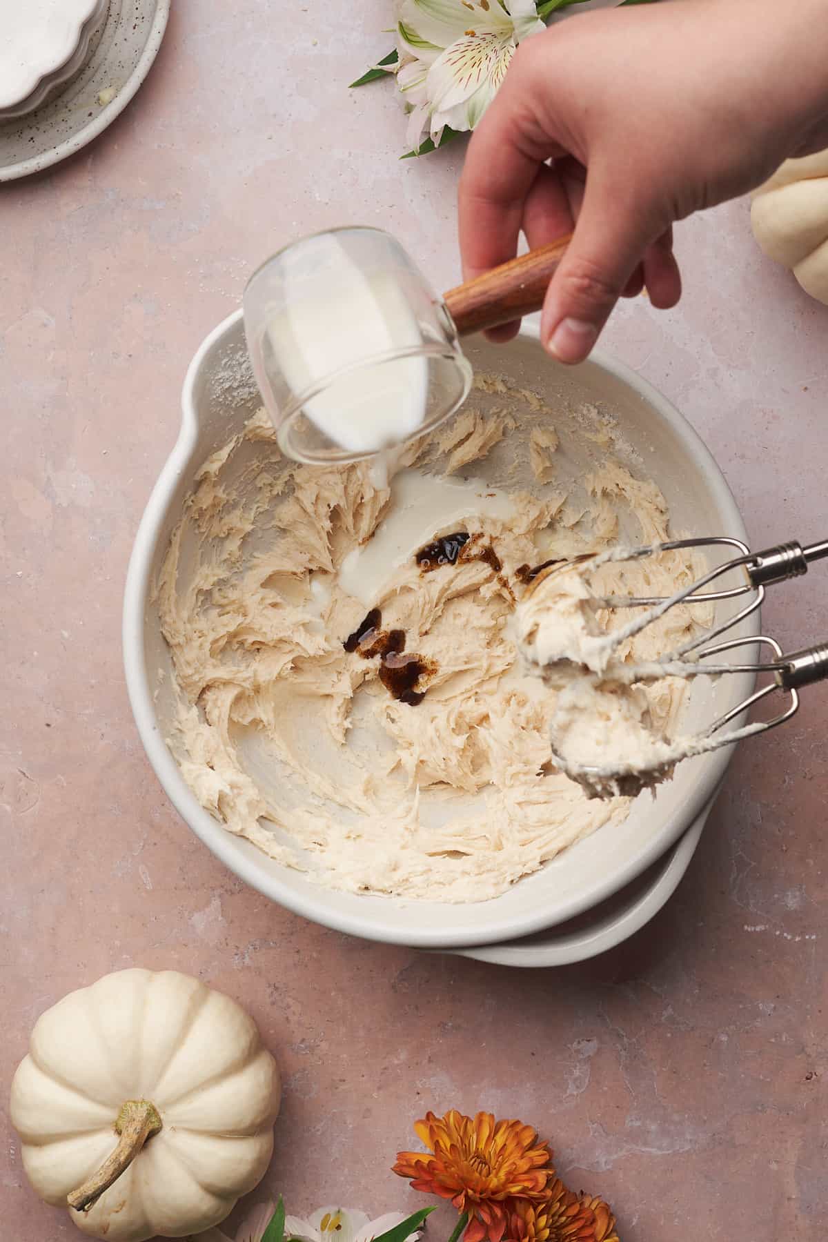 hand pouring in milk into a bowl with vanilla, and a cream cheese frosting. 