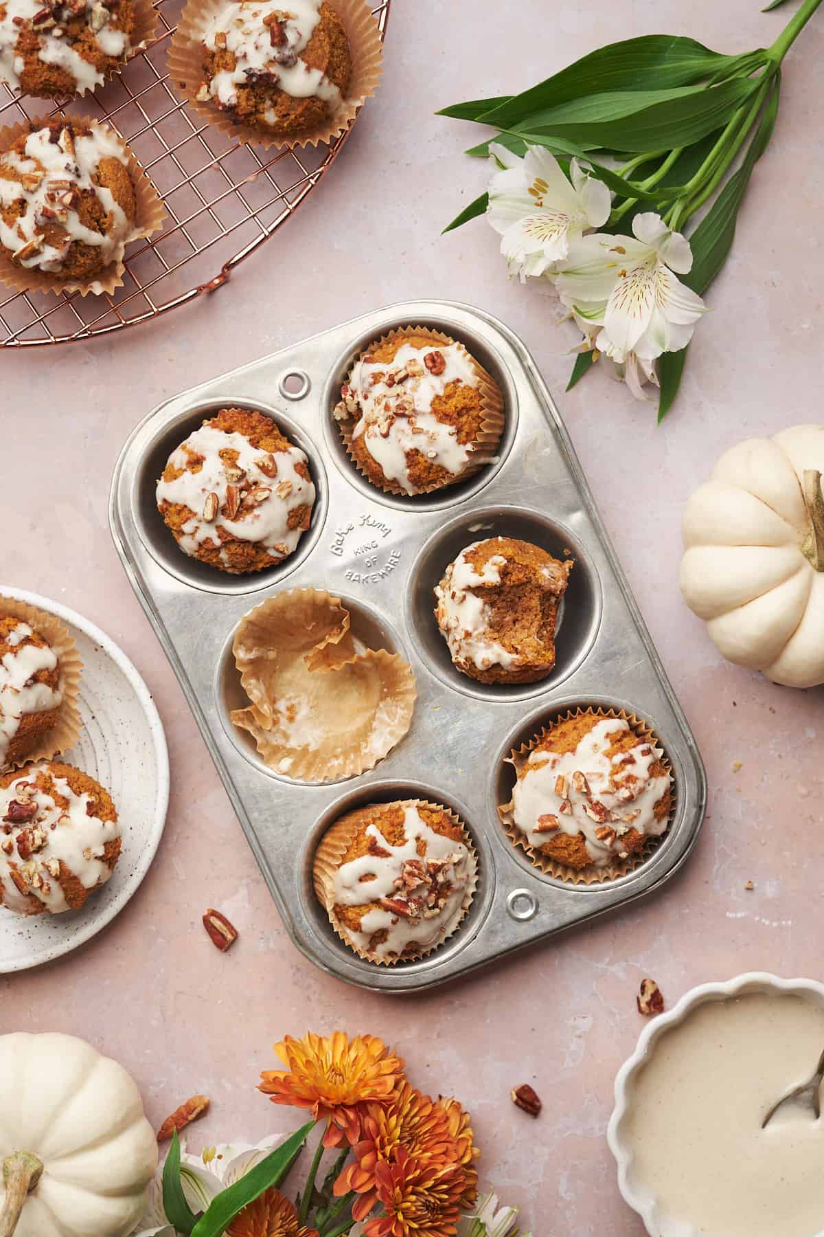 keto pumpkin muffins in a metal tin, topped with cream cheese glaze and pecans. 