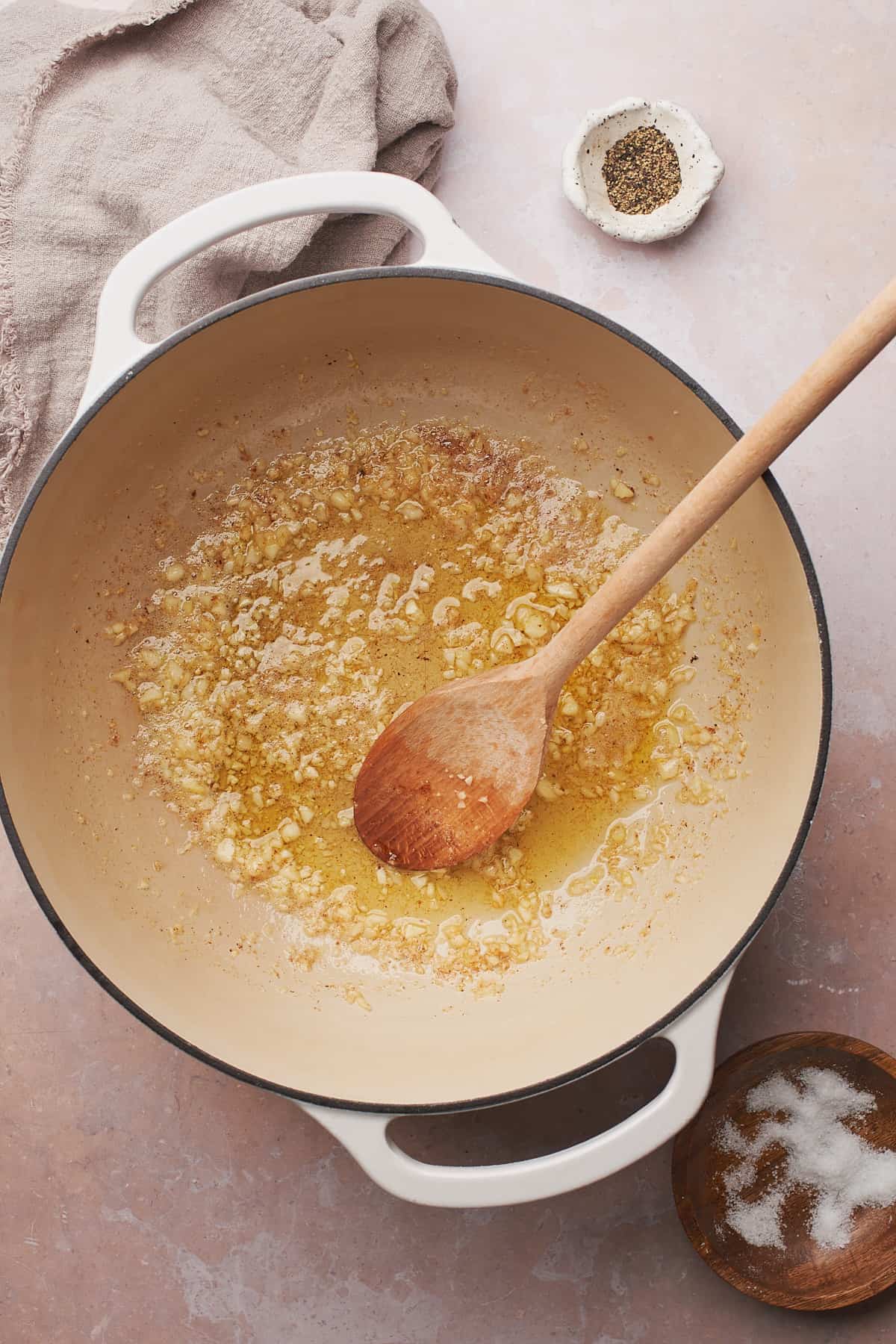 garlic cooking in a dutch oven with butter, and wooden spoon in the pot. 