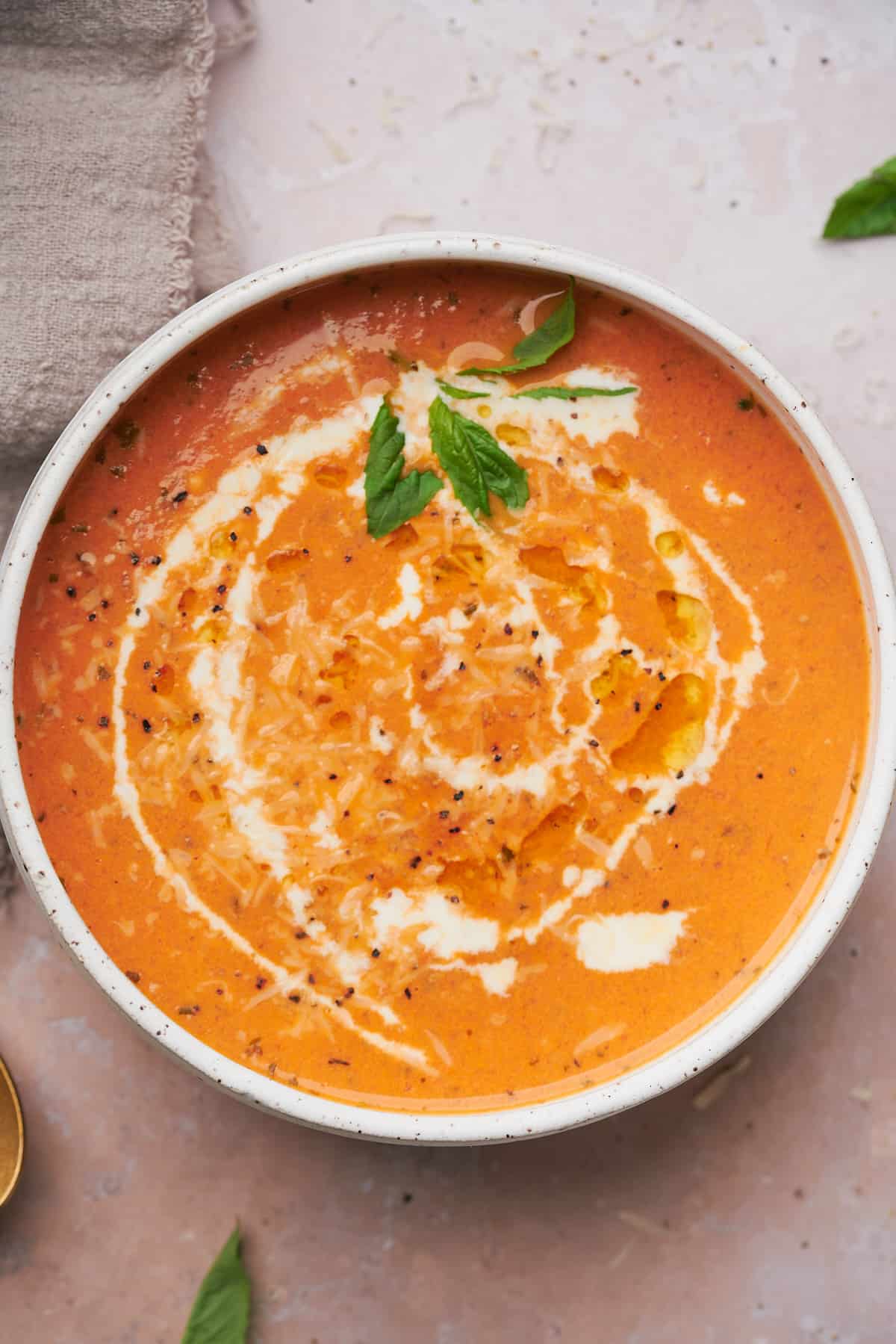 close up shot of keto tomato soup drizzled with heavy cream, olive oil, fresh pepper, parmesan, and basil. 