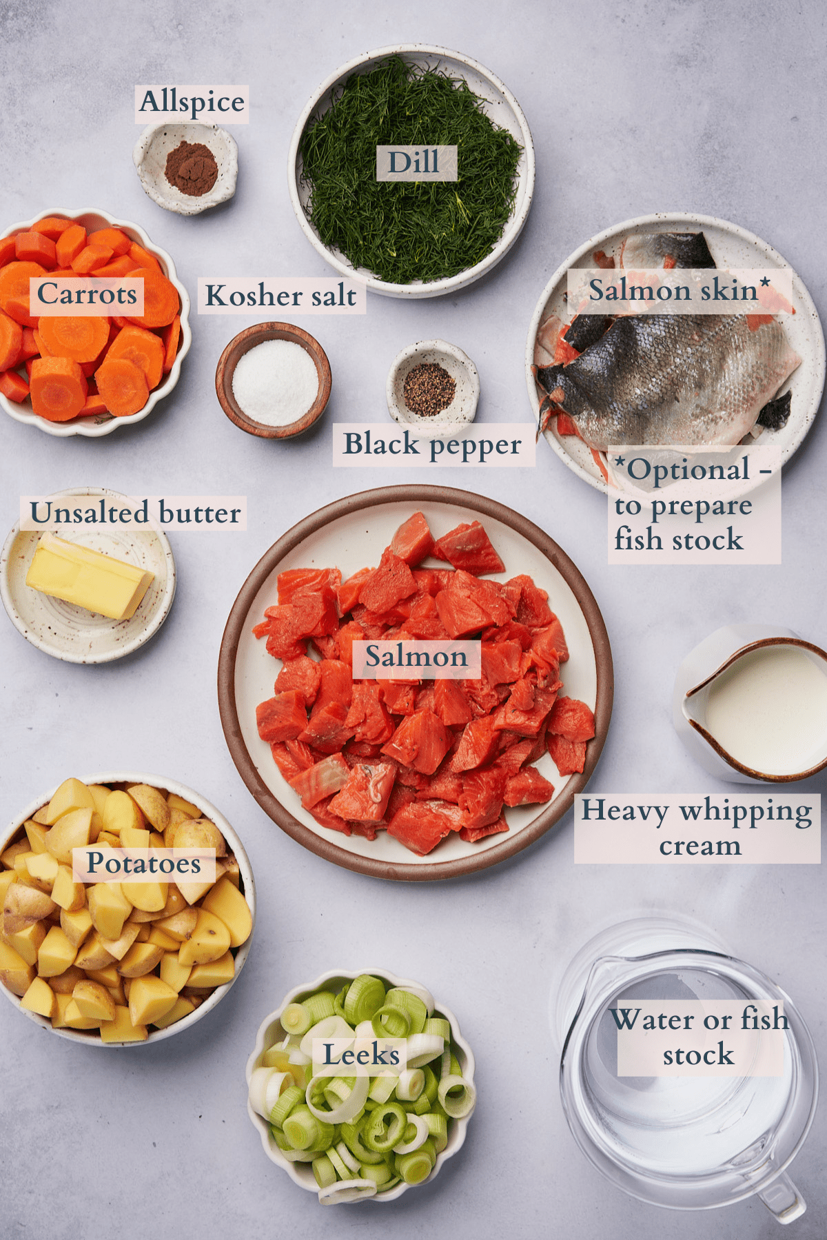 ingredients to make a salmon soup, with different ingredients laid out in ceramic bowls and on plates. 