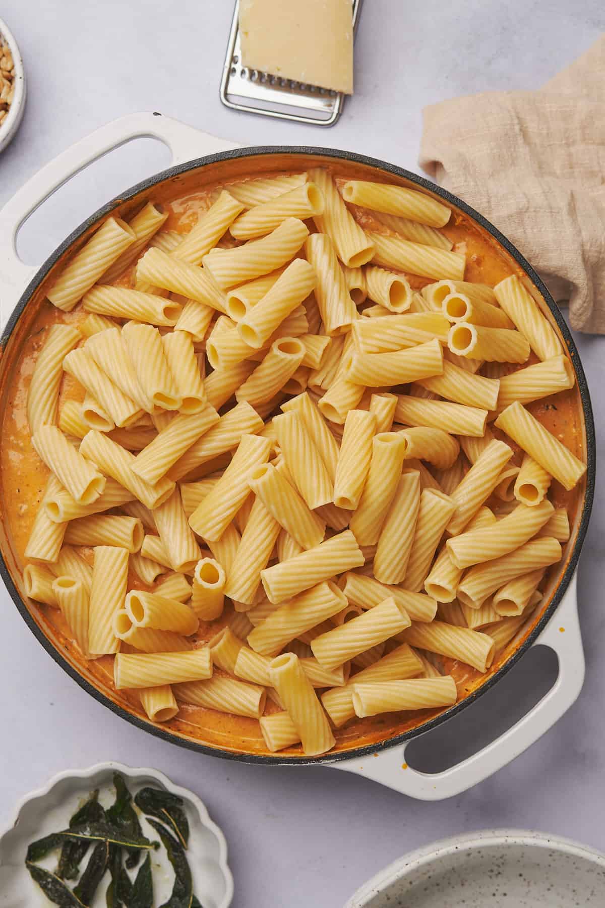 cooked rigatoni pasta added to pumpkin sauce in a skillet. 
