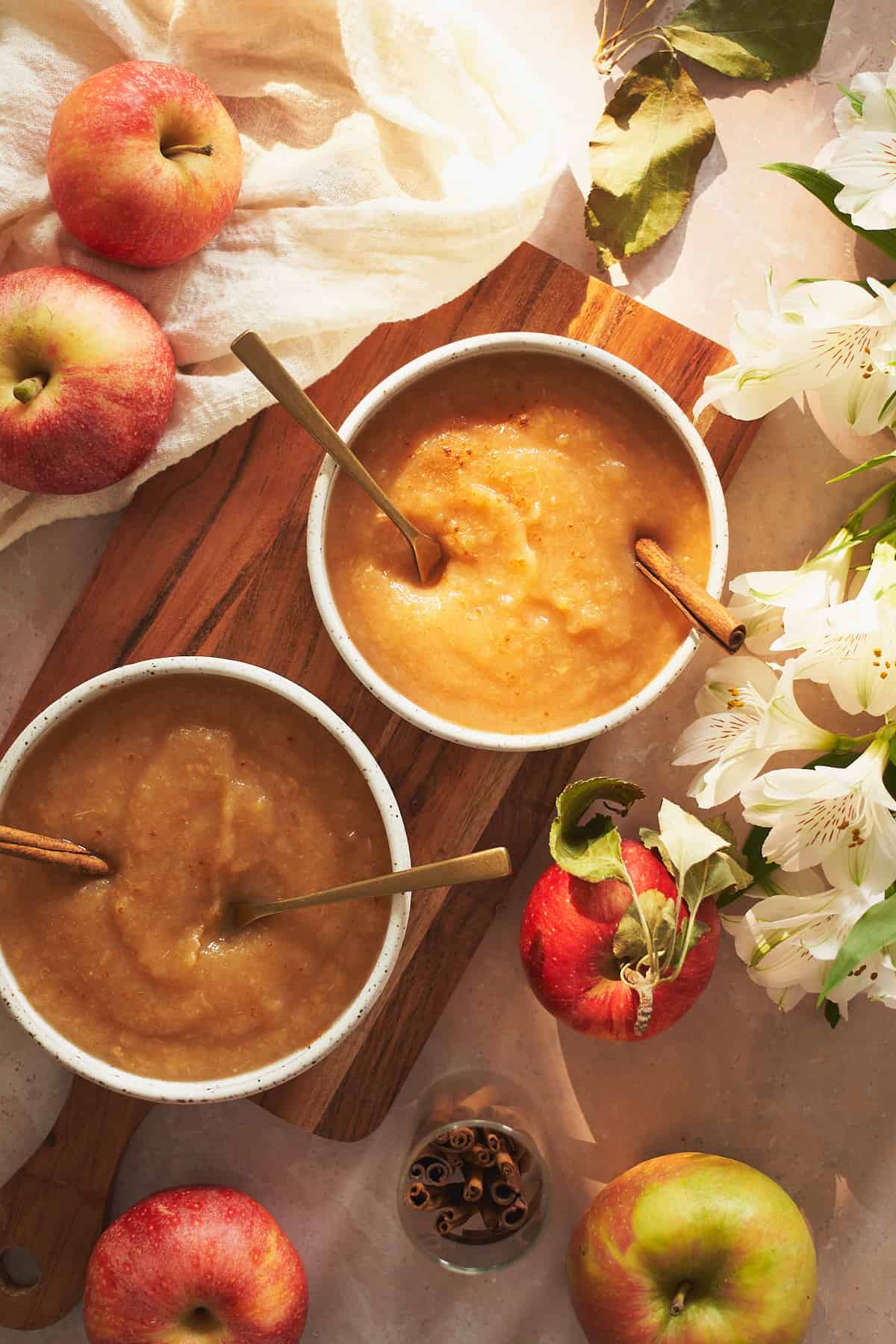 stunning natural light bowls of applesauce with flowers, apples, and cinnamon surrounding the scene. 