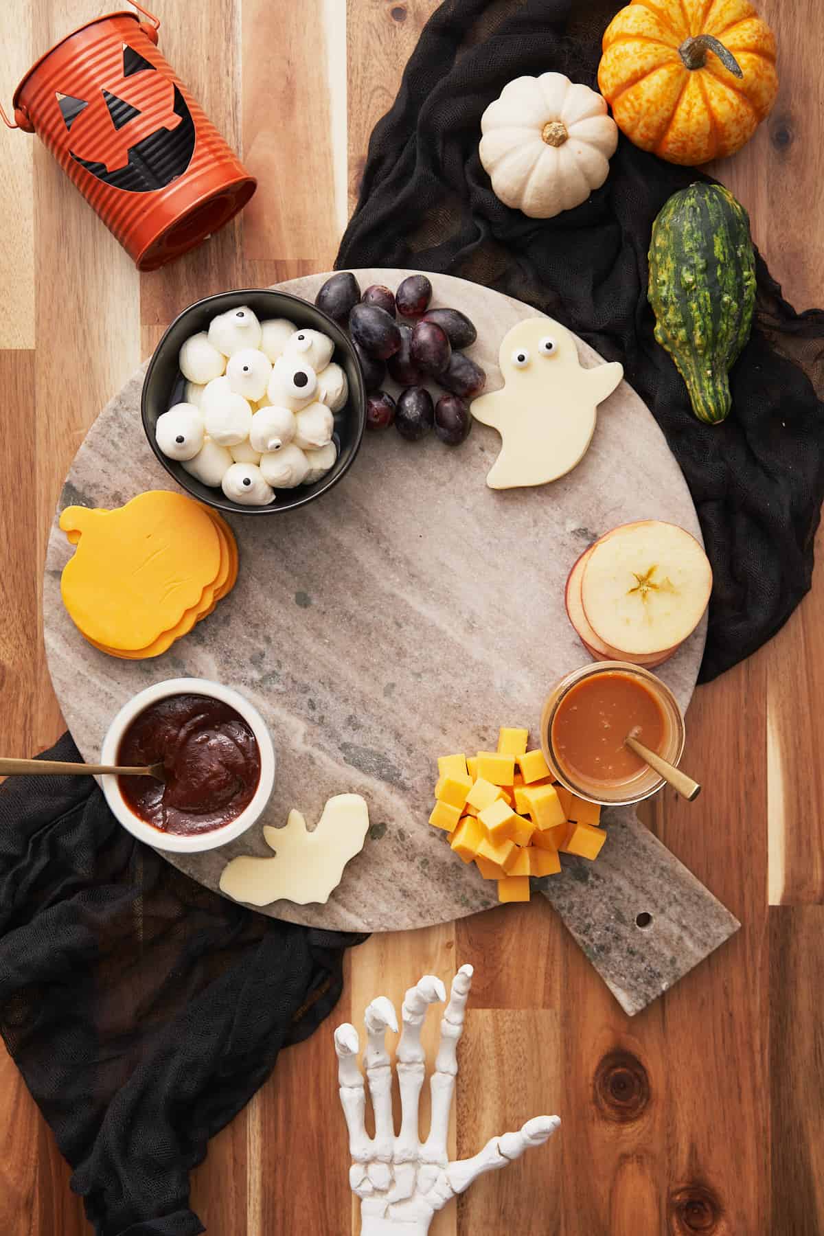 building a halloween charcuterie board with bat shaped, pumpkin shaped, and ghost shaped cheese, along with grapes and apple rounds.