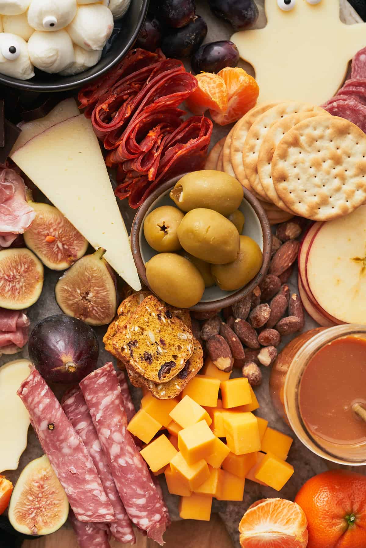 close up shot of a charcuterie board for Halloween, with  cheese, meat, caramel sauce, apple slices, olives, figs, and more. 