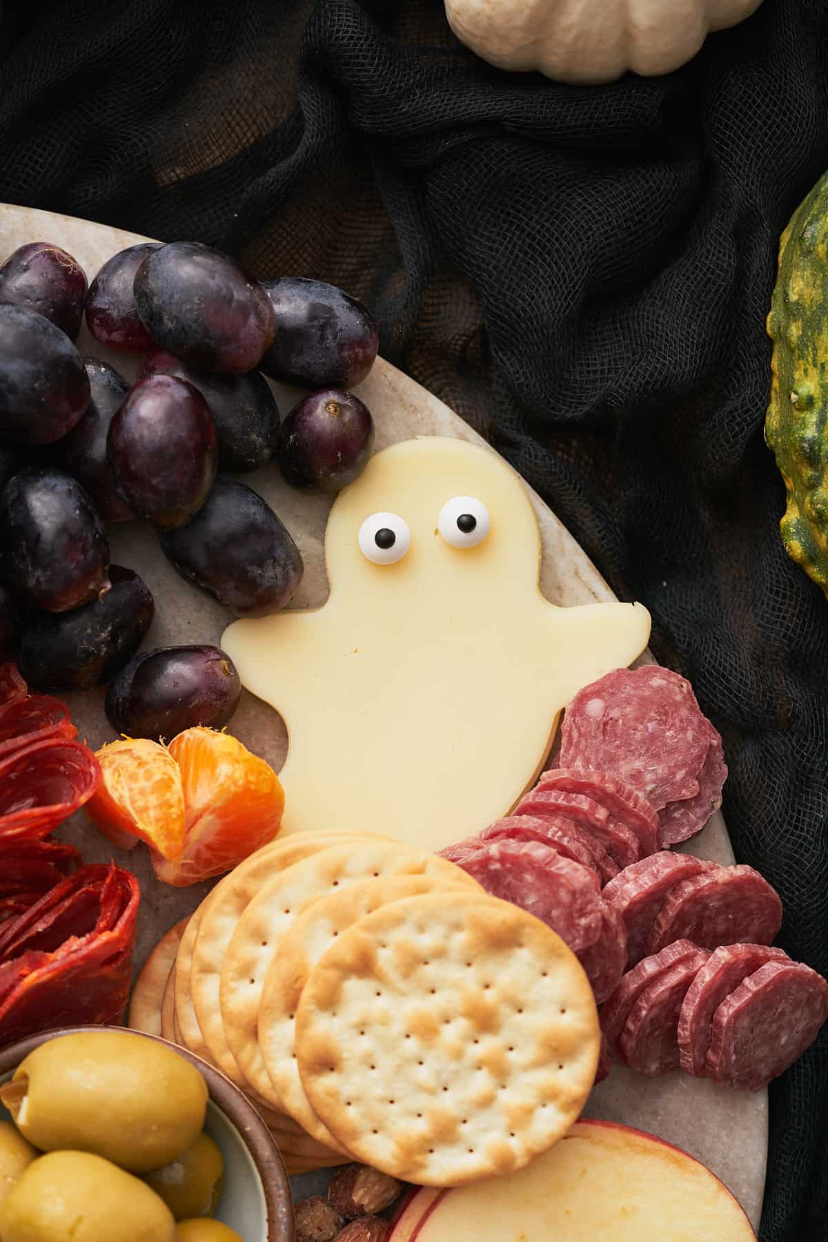 spooky provolone cheese ghost with candy eyeballs, near black grapes, cured salami bites and crackers.