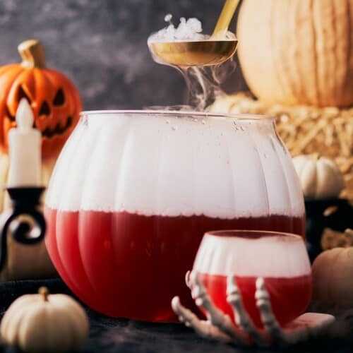 spooky Halloween punch in a large punch bowl, with a gold ladle, bubbling dry ice, and jackolanterns.