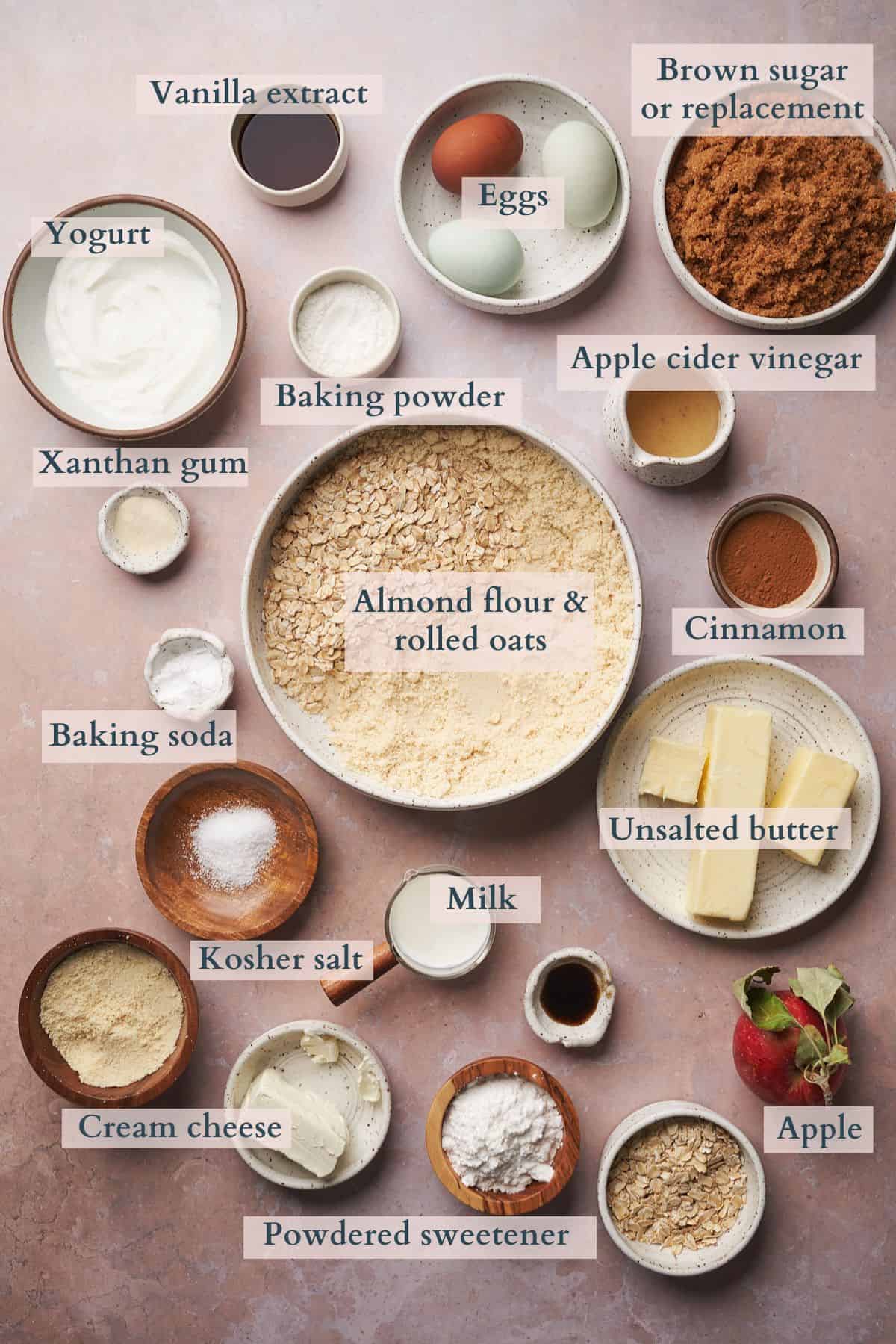ingredients to make apple muffins laid out in ceramic bowls, with text overlaying to denote each ingredient. 