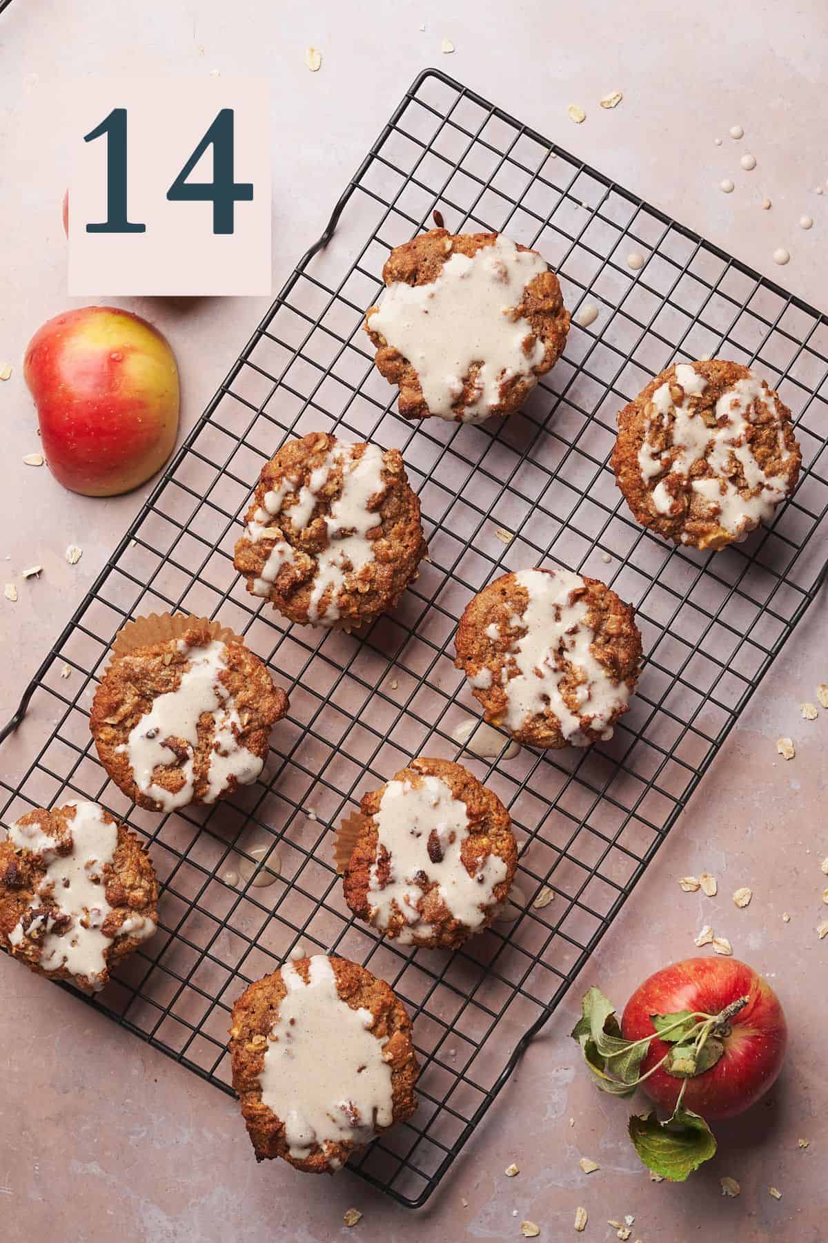 apple muffins topped with a cream cheese glaze, with apples on the sides of the wire rack. 