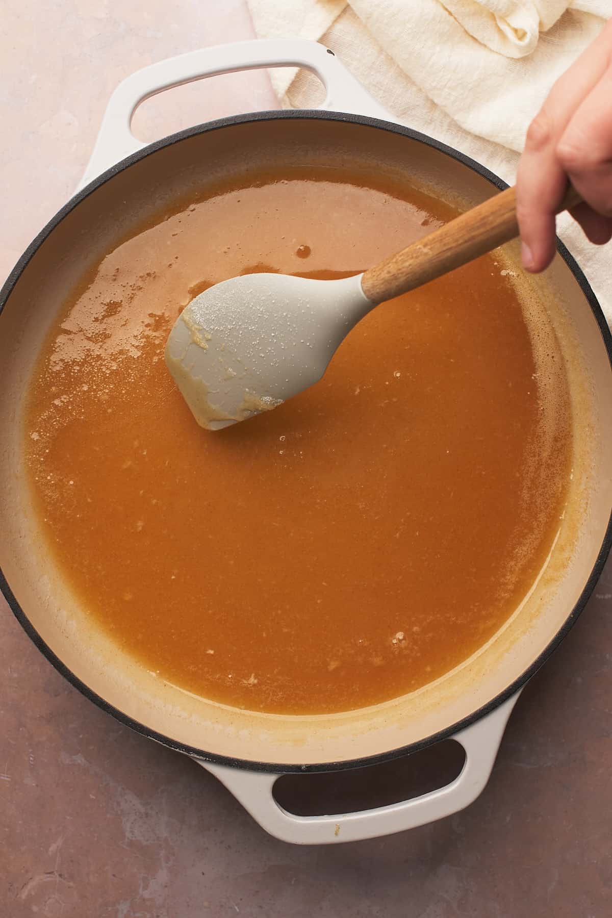 hand with a rubber spatula stirring a caramel mixture in an enameled dutch oven. 