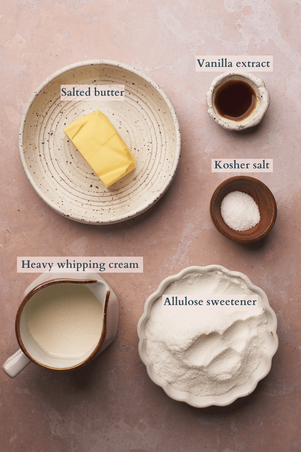 ingredients to make keto salted caramel sauce laid out in bowls, with text overlaying to denote salted butter, allulose sweetener, kosher salt, heavy whipping cream and vanilla extract. 