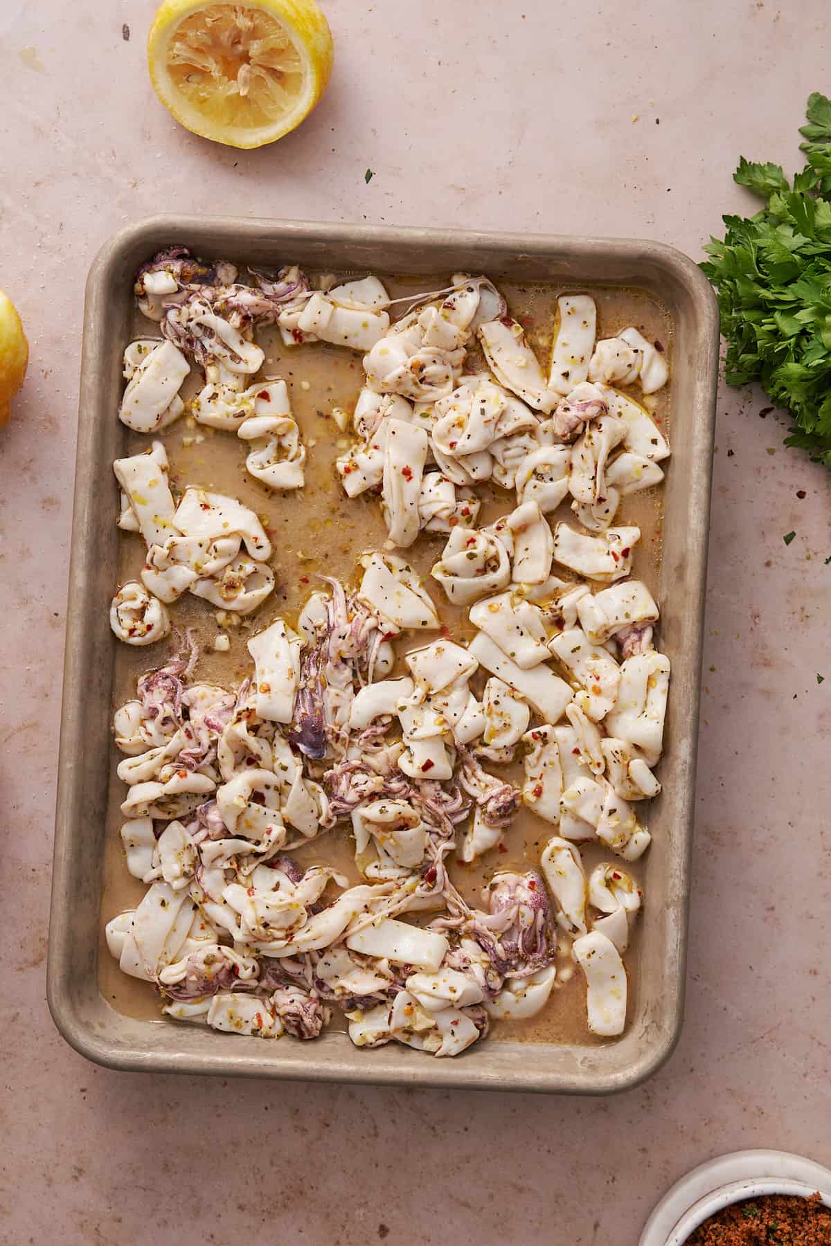 calamari on a baking sheet with seasonings, olive oil, and lemond juice. 