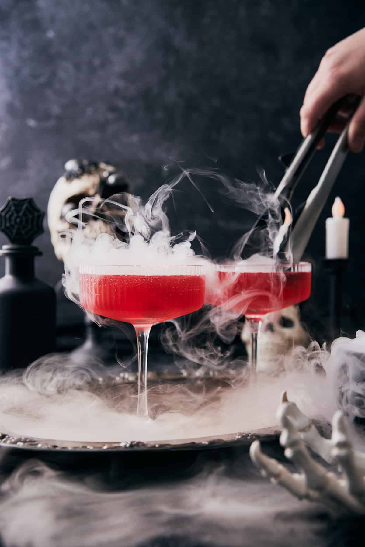 hand placing a dry ice cube into a martini glass with smoke spilling out of the cocktail. 